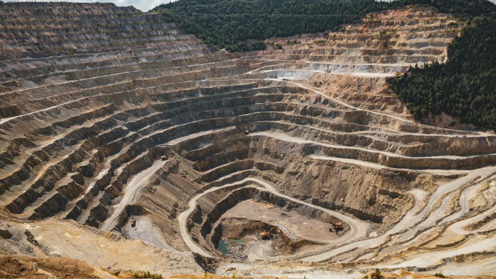 Open-pit mine with terraced excavation and surrounding forest.