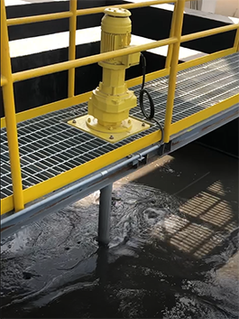 Yellow motor mounted on a grated walkway above dark water in an industrial setting