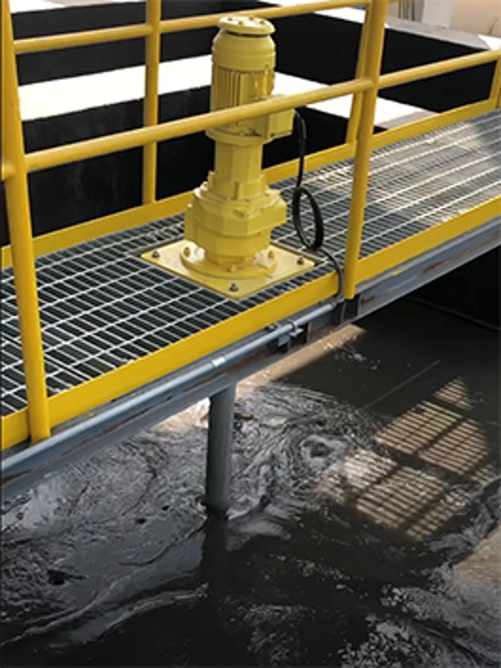 Yellow motor mounted on a grated walkway above dark water in an industrial setting