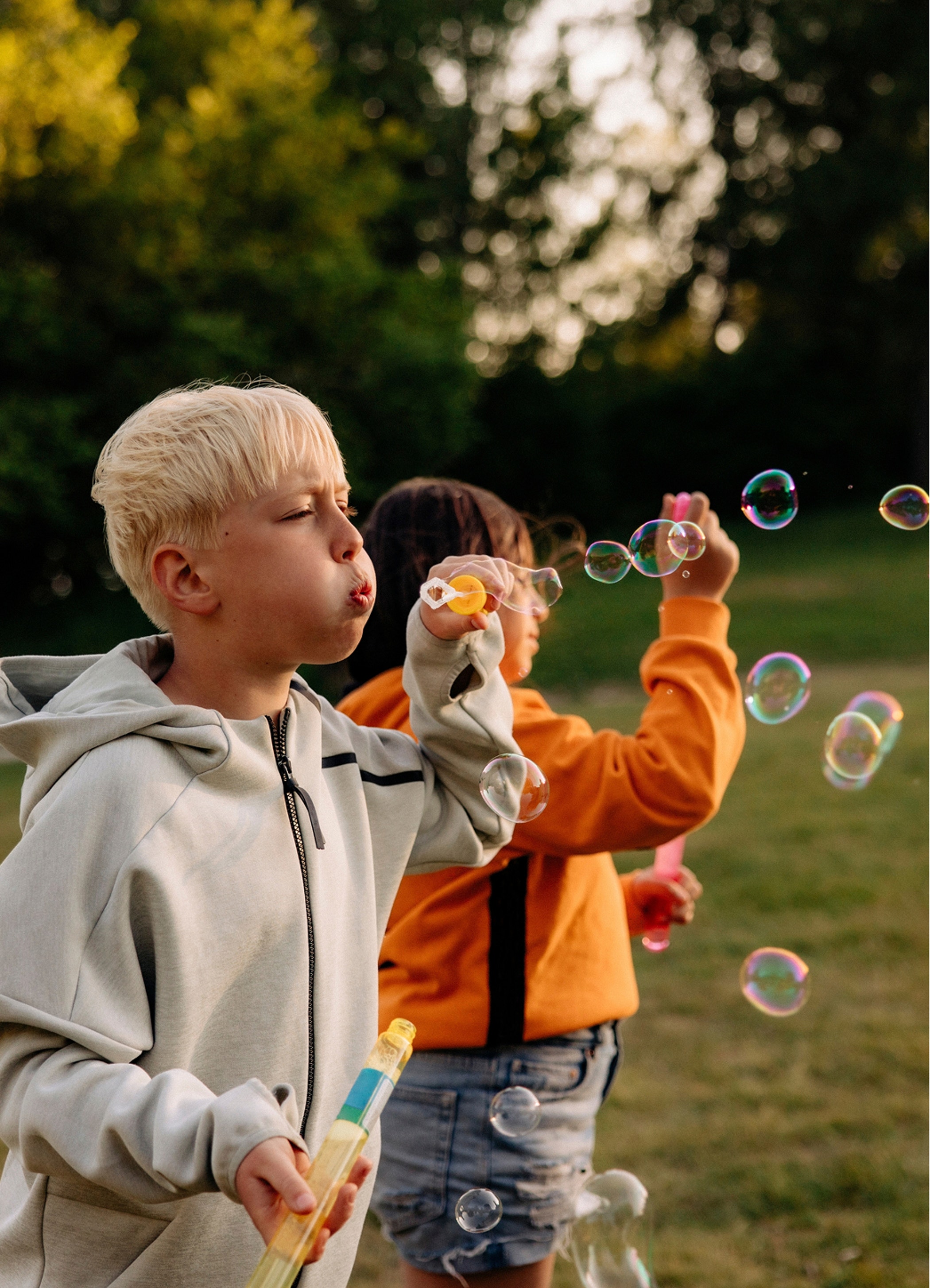 Boy blowing bubbles with female friend standing in playground at summer camp