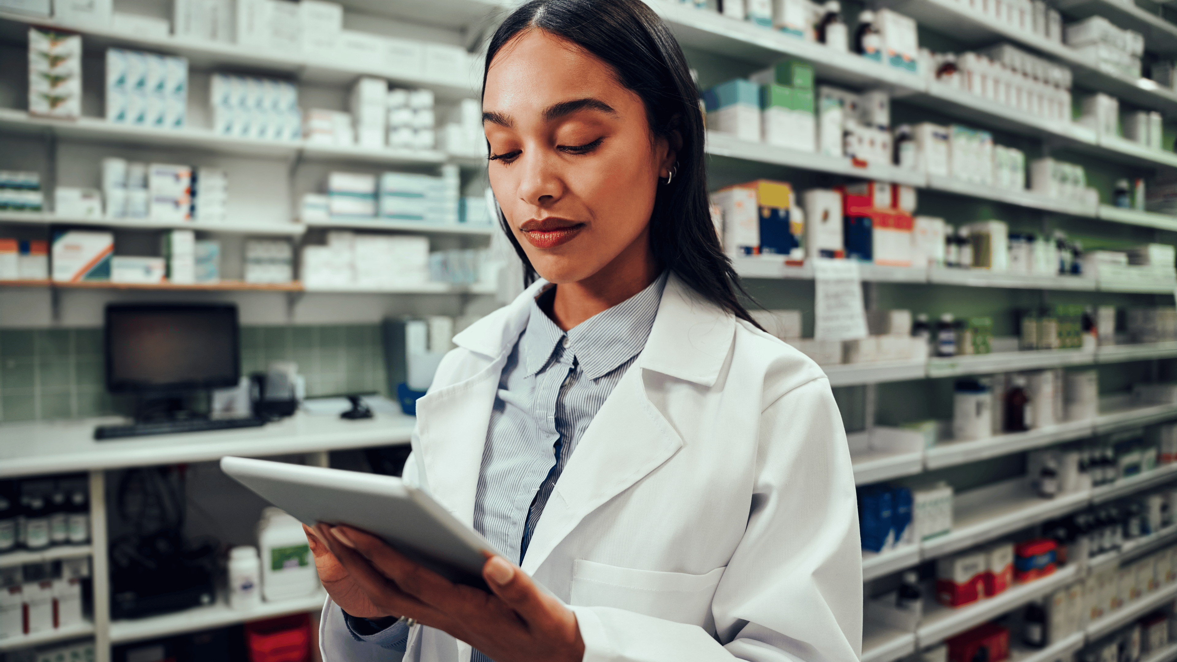 Young female pharmacist working using digital tablet standing in chemist wearing labcoat.