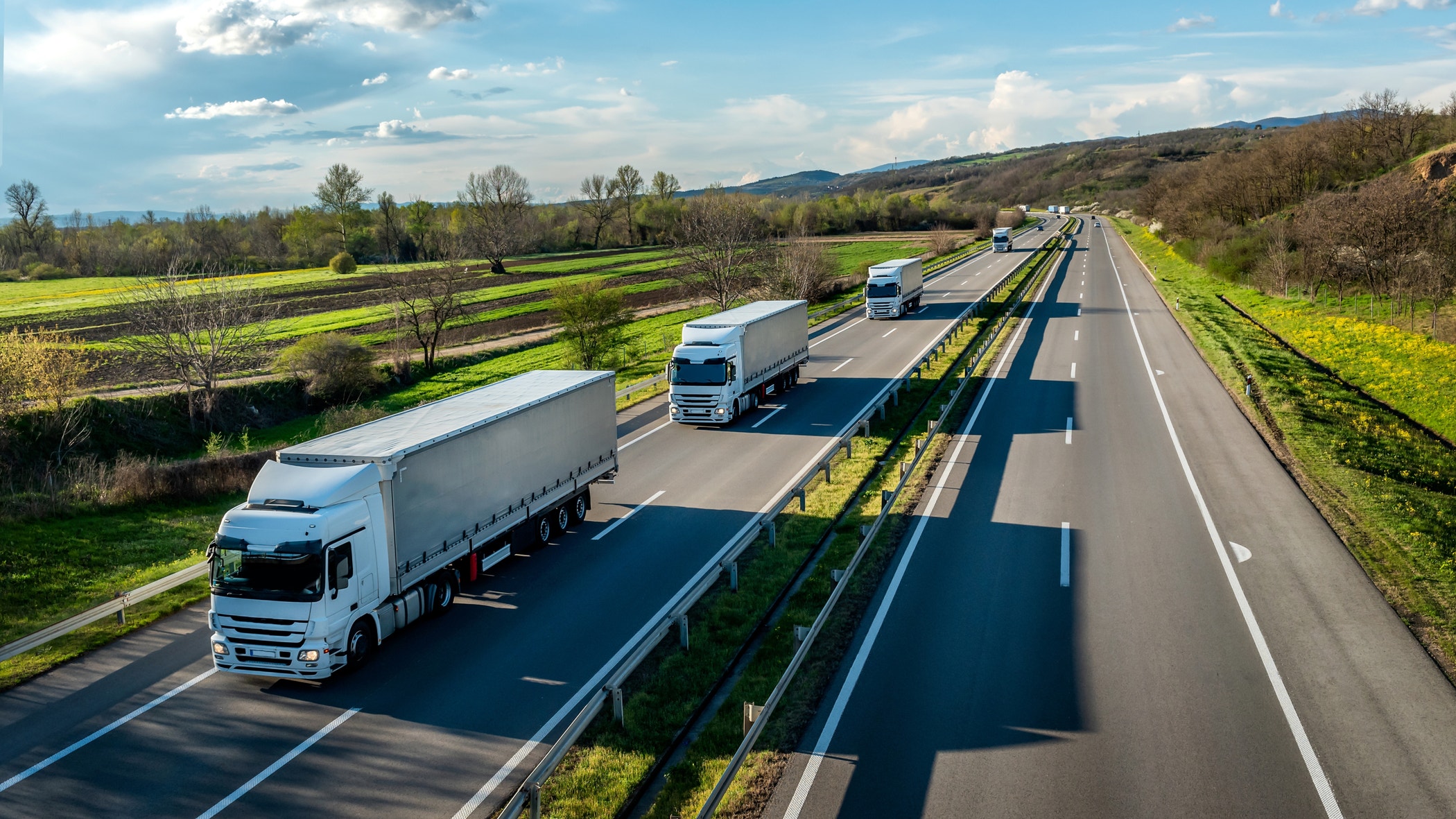Convoy of white trucks with containers on highway, cargo transportation concept at sunset.