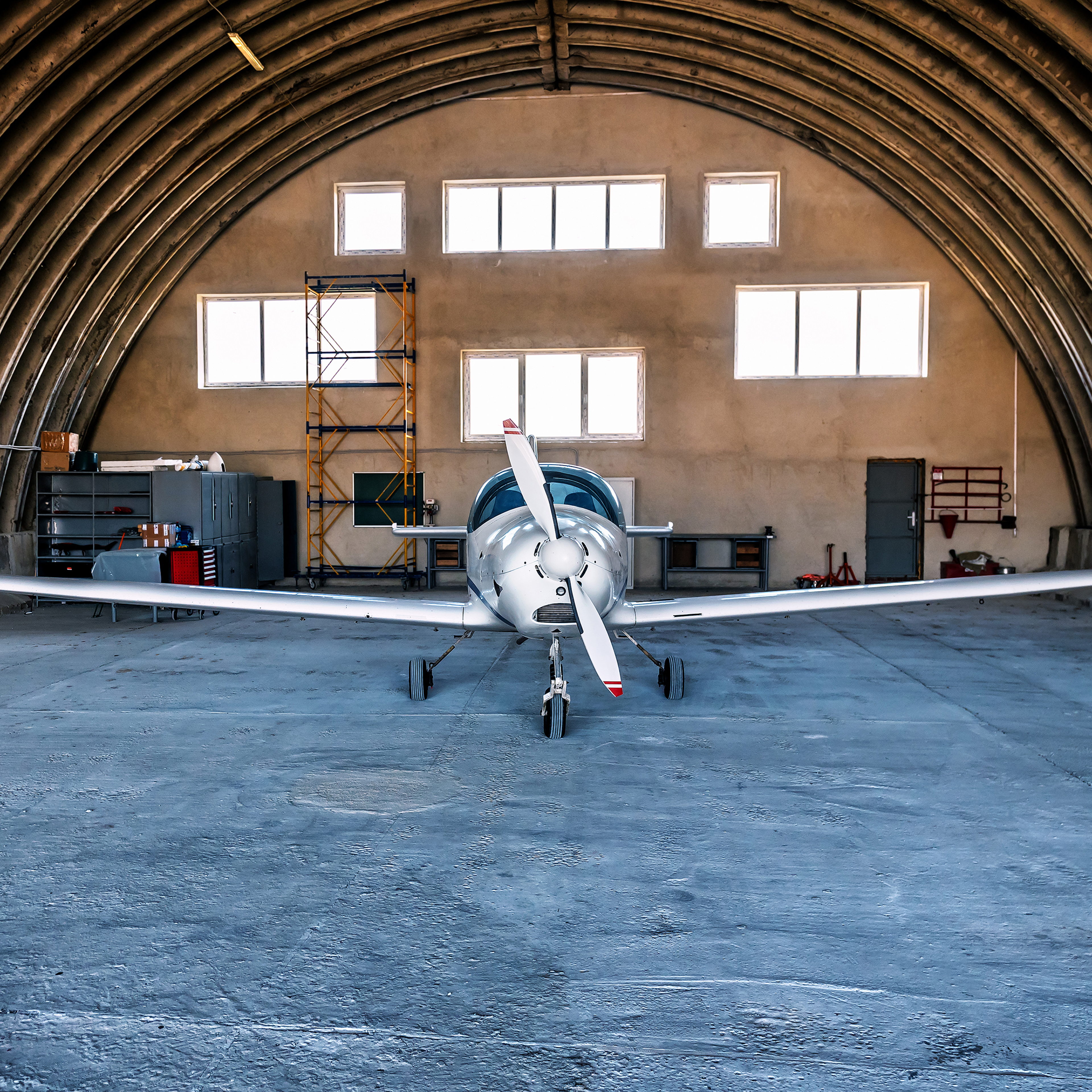 A plane is parked inside a hangar, with a person nearby. The hangar has a high ceiling and is well-lit, showcasing the aircraft on the ground.