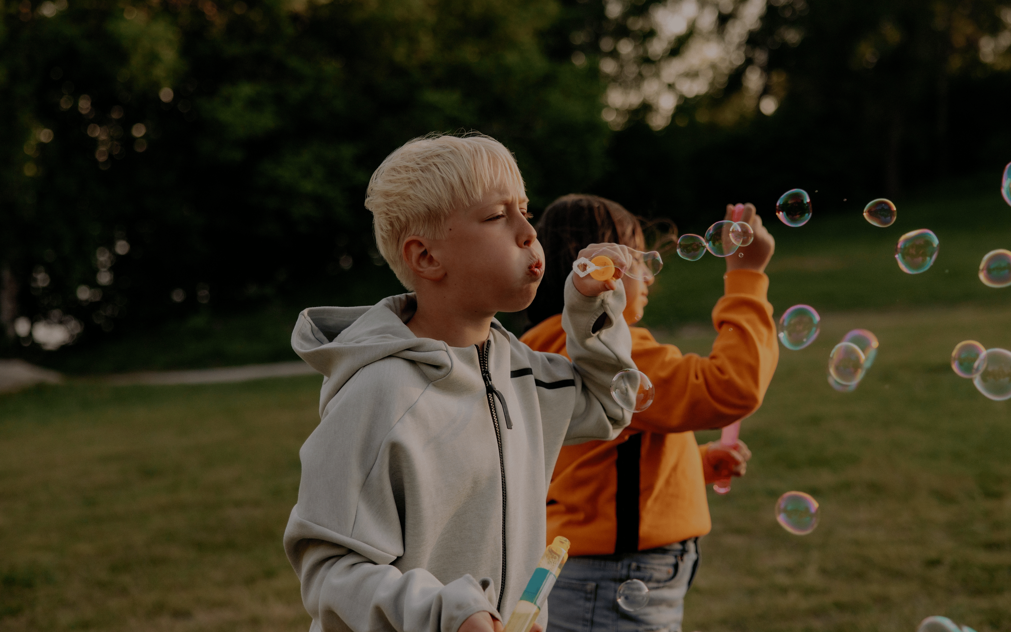 Boy blowing bubbles with female friend standing in playground at summer camp