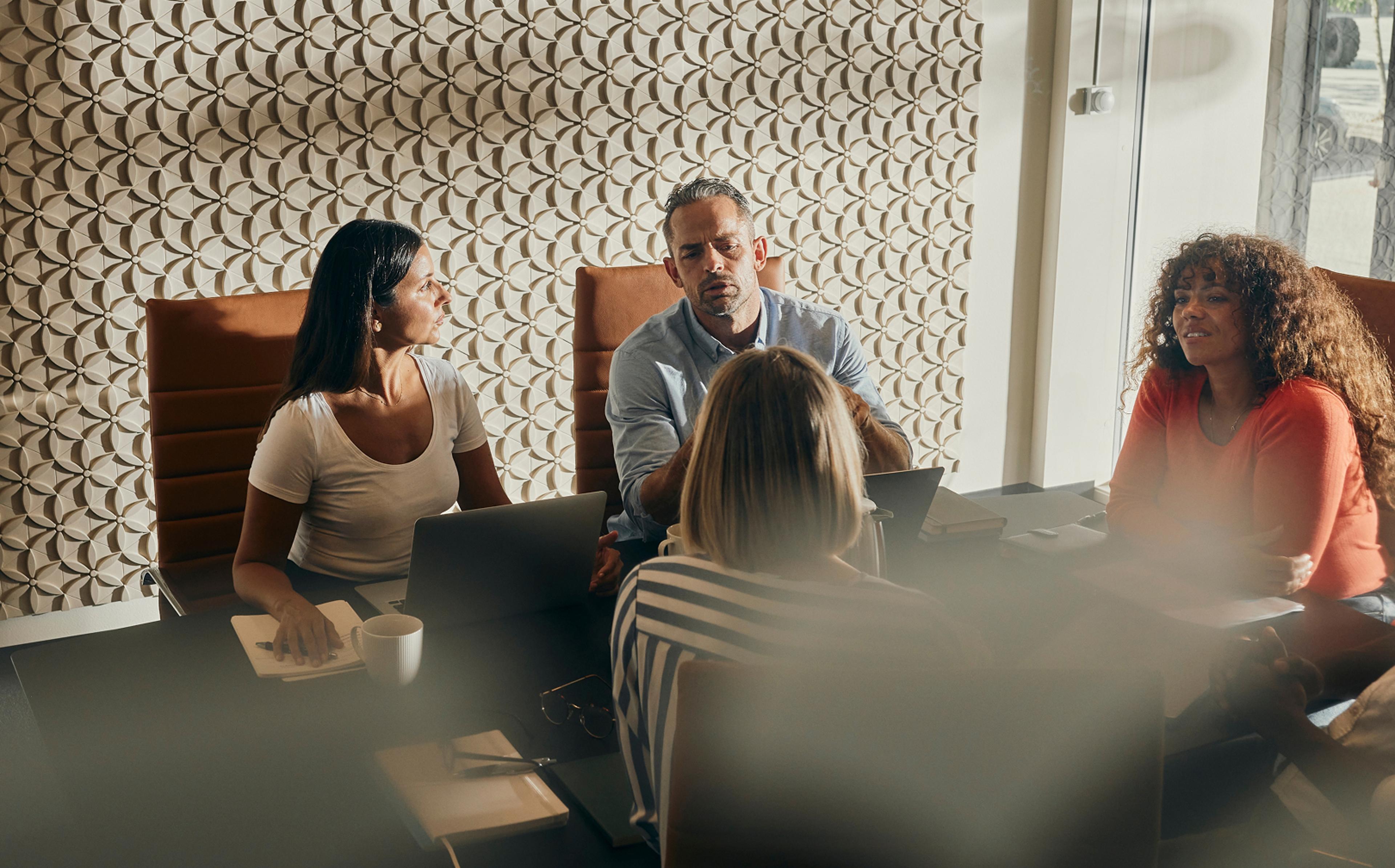 A diverse group of professionals actively participating in a business meeting. They are seated around a table in a modern office setting, emphasizing teamwork, collaboration, and productivity.