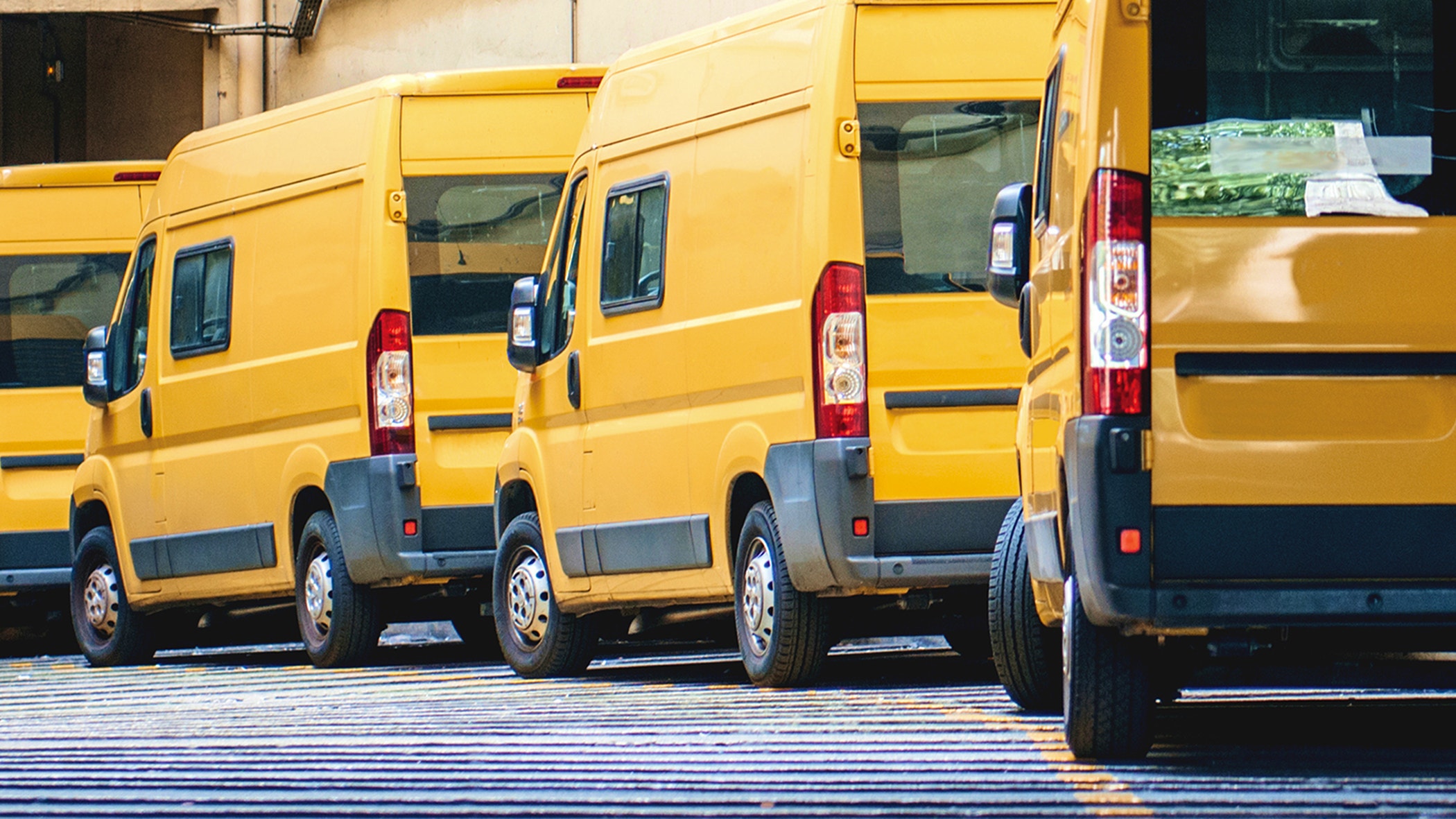 Yellow delivery vans in a row service van, trucks and cars in front of the entrance of a warehouse distribution logistic plant.