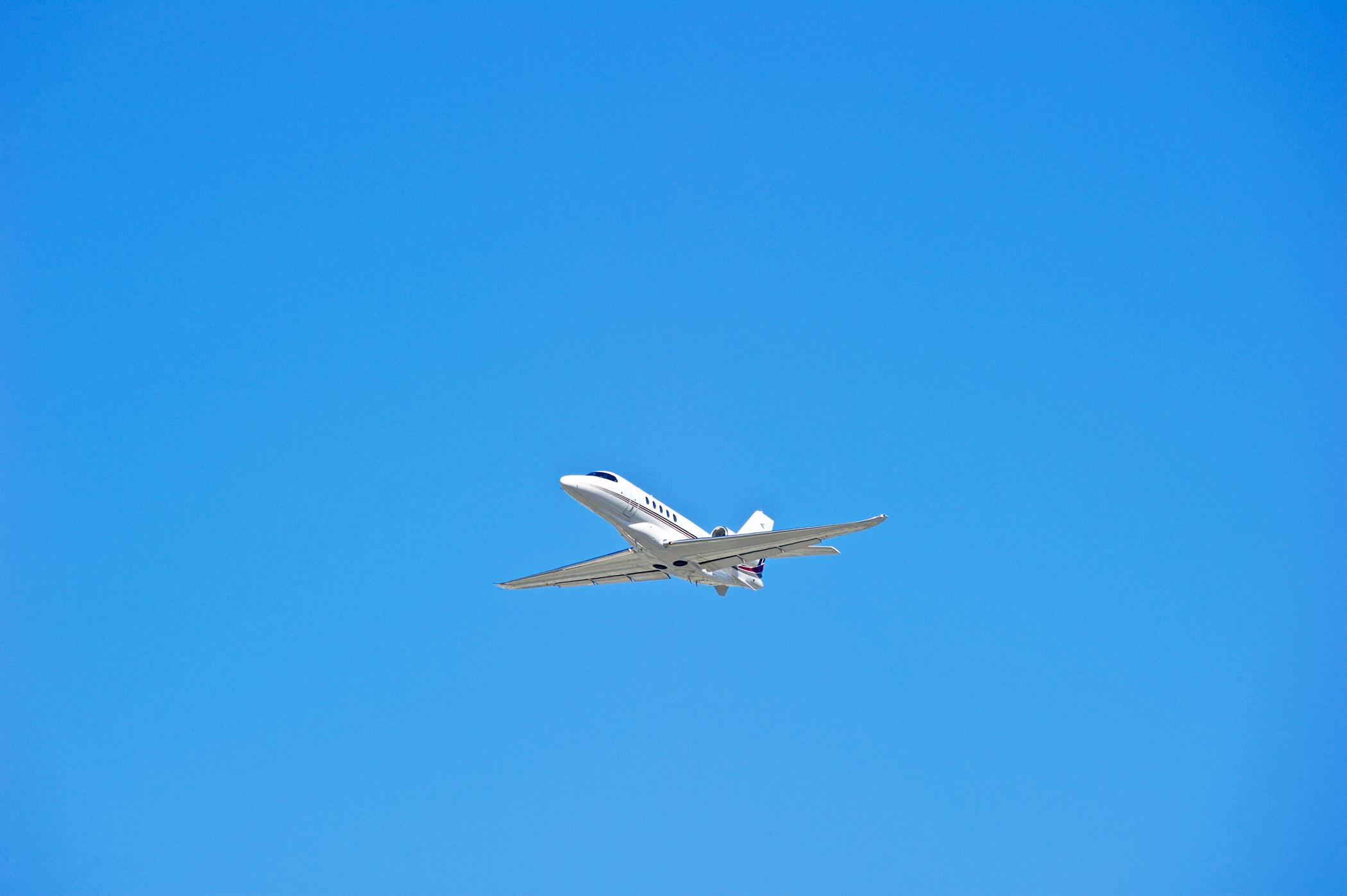 A low-angle shot of a white private jet flying across a clear, bright blue sky