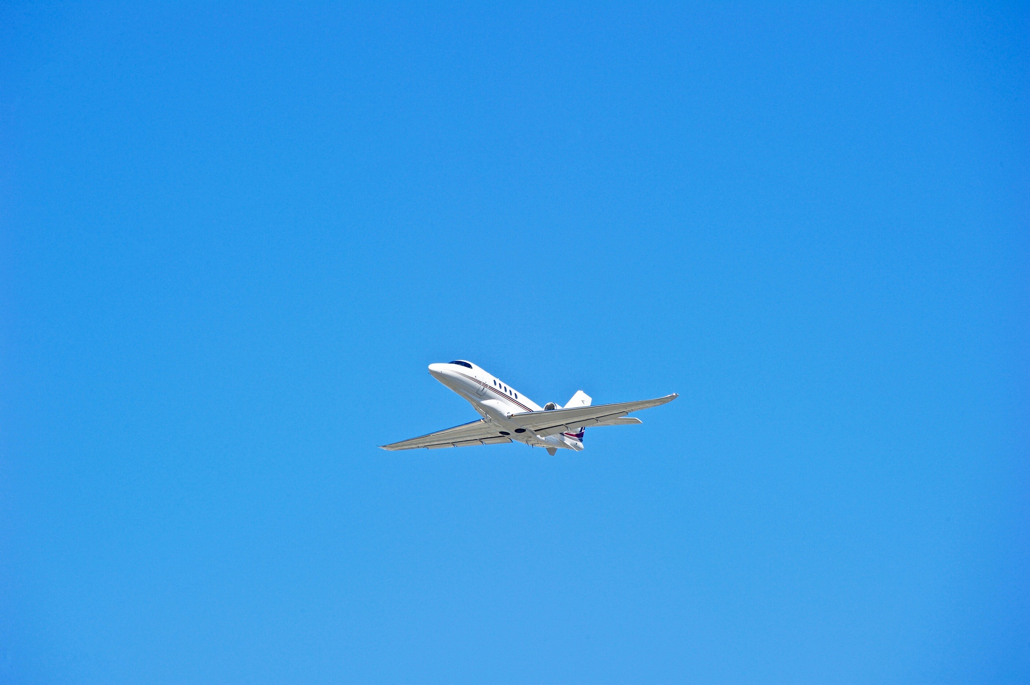 A low-angle shot of a white private jet flying across a clear, bright blue sky