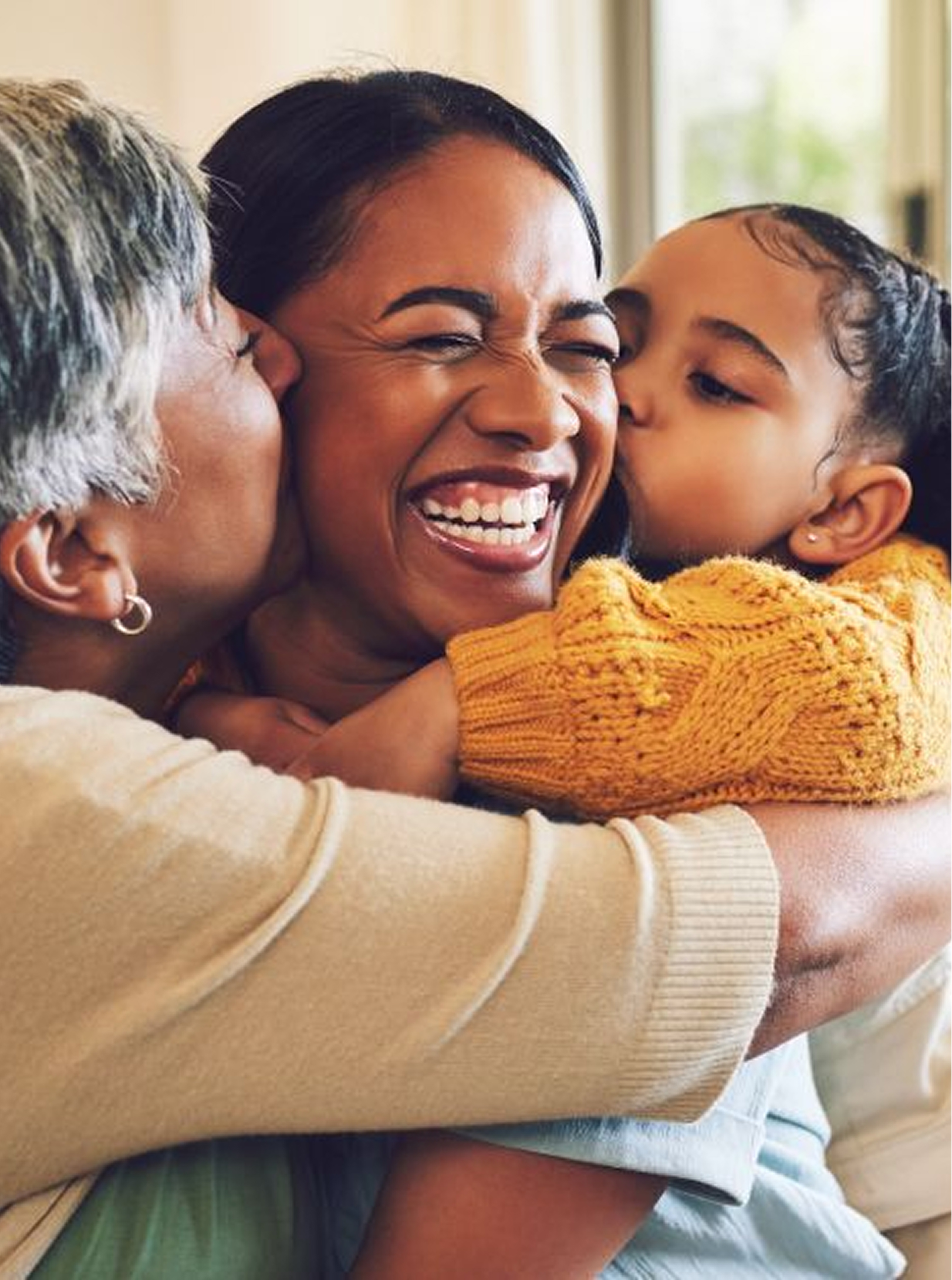 Three generations lovingly embrace, showcasing family togetherness and happiness. A child and elderly woman kiss a joyful woman.