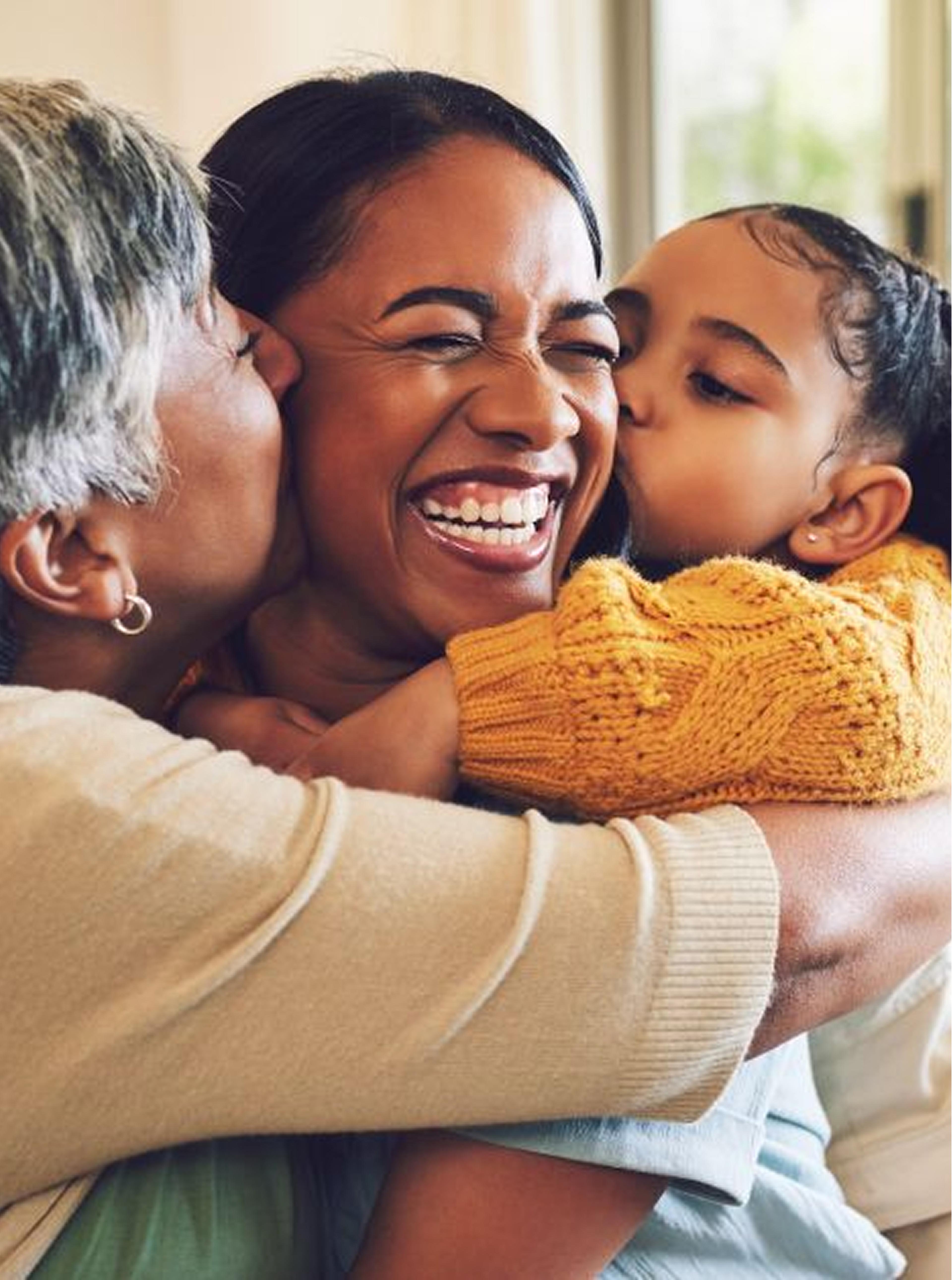 Three generations lovingly embrace, showcasing family togetherness and happiness. A child and elderly woman kiss a joyful woman.