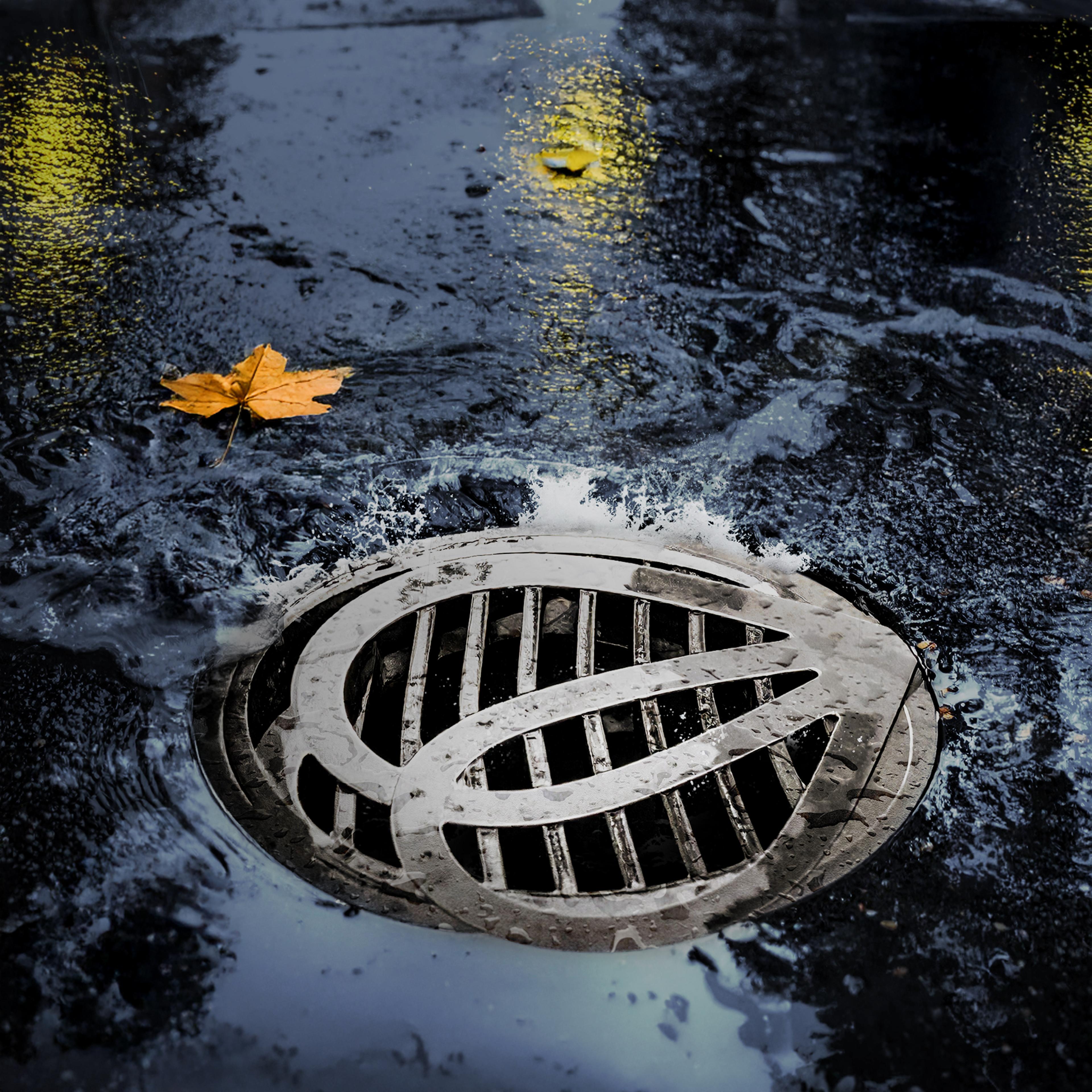 Water flowing into a metal street drain with a circular grate design on a wet asphalt surface.