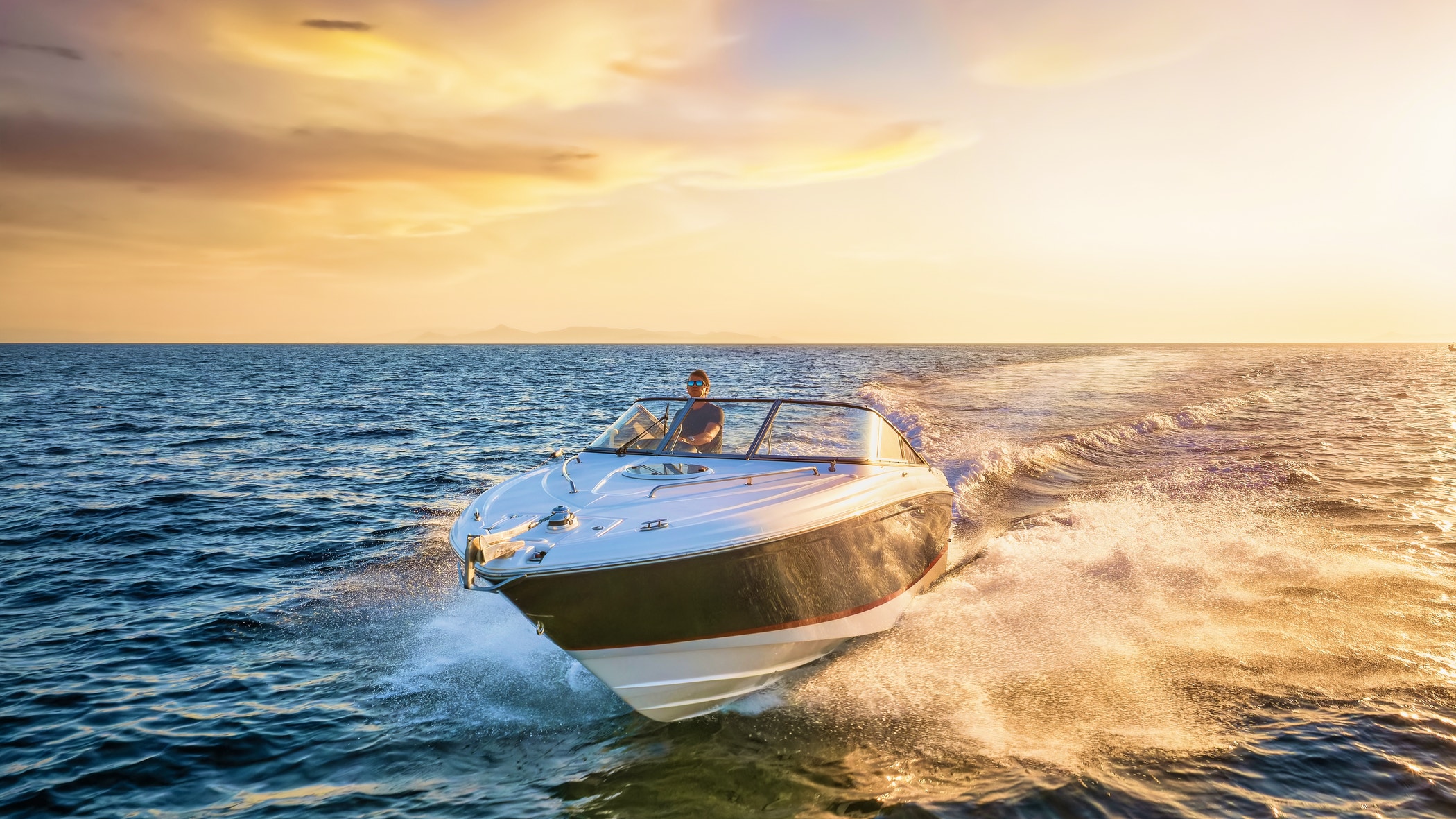 Front view of a sports motor boat cruising with high speed over the blue sea during summer sunset time.