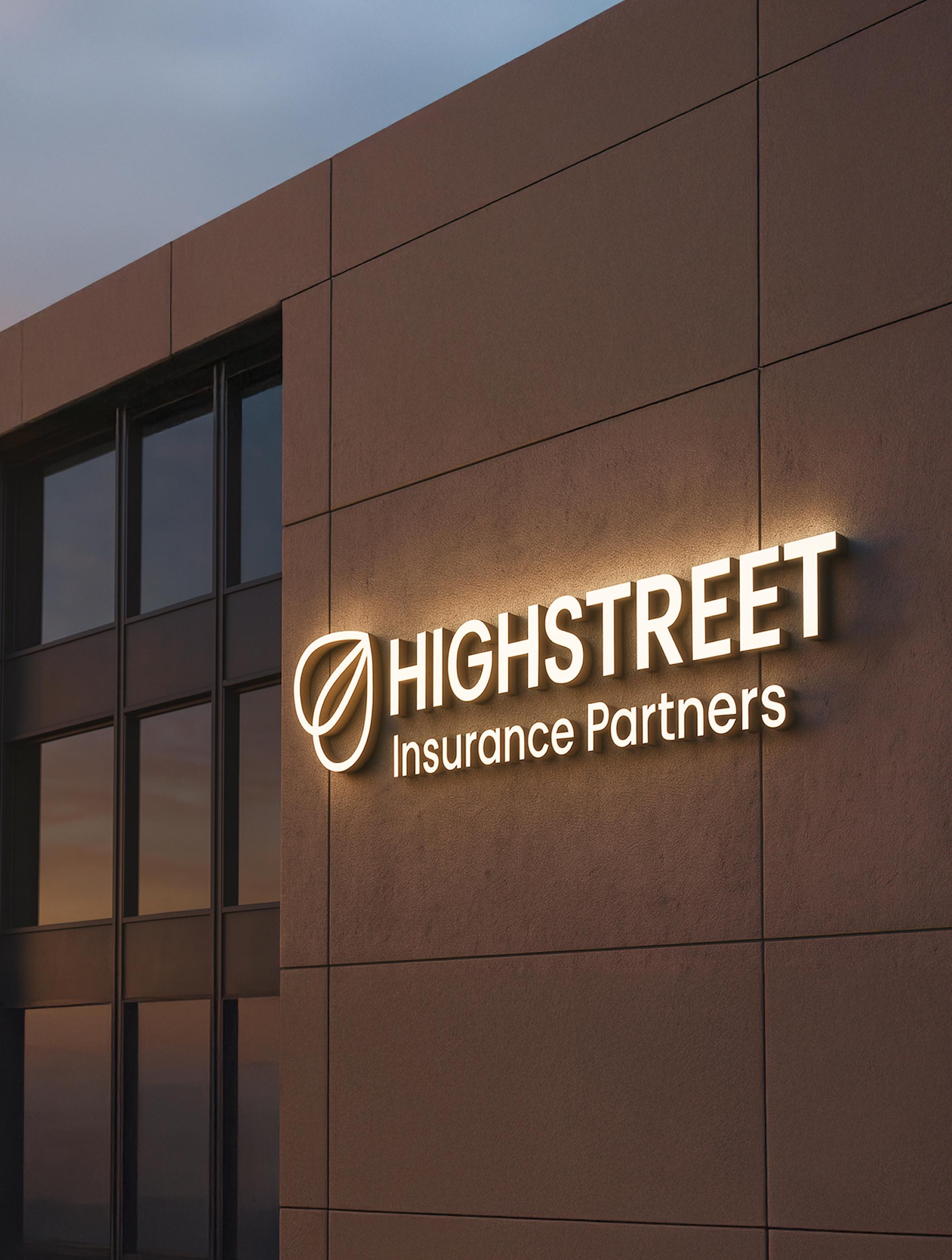 Building exterior with illuminated signage reading “Highstreet Insurance Partners” at dusk.