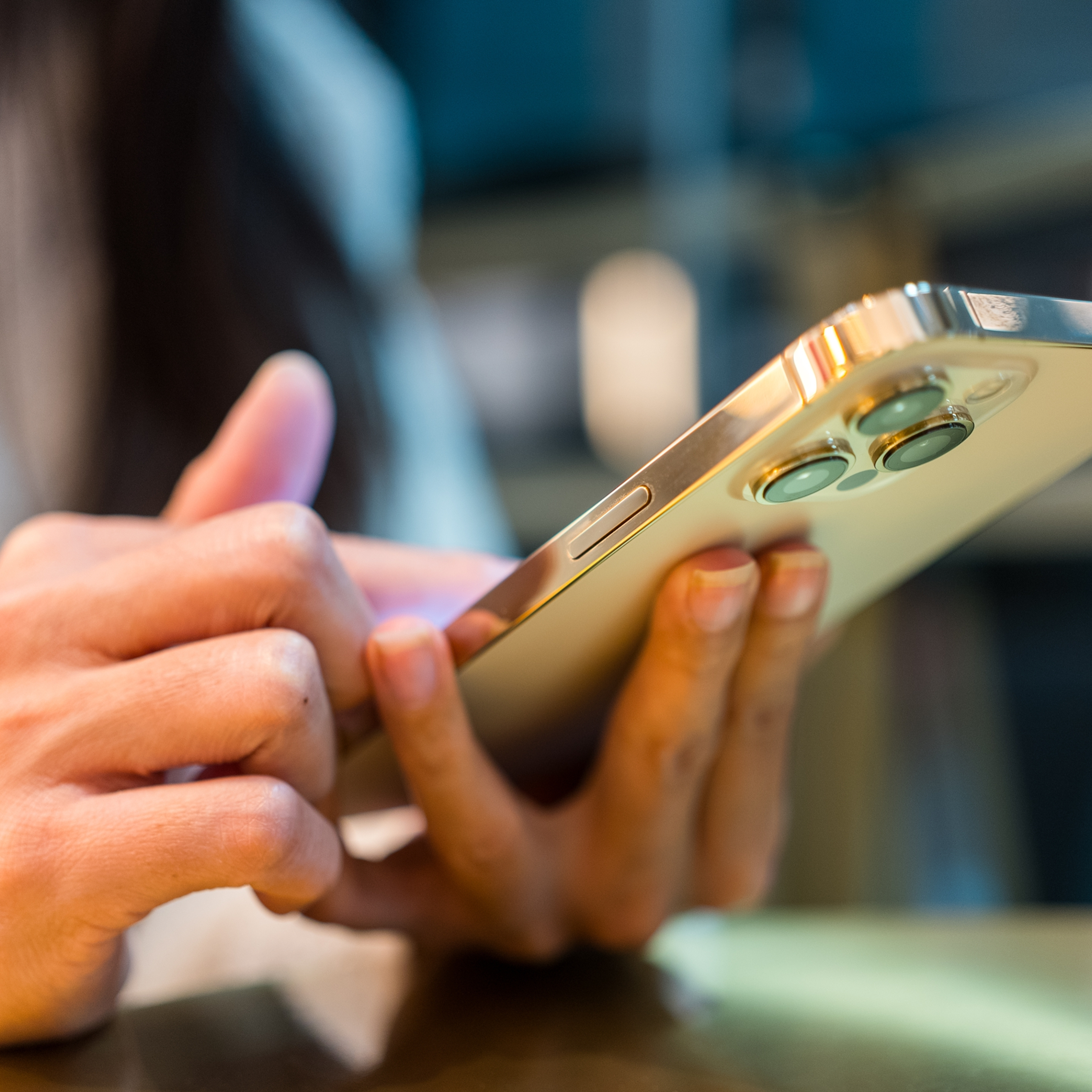 A person holding and using a modern smartphone with a metallic finish, focusing on their hands and the device.