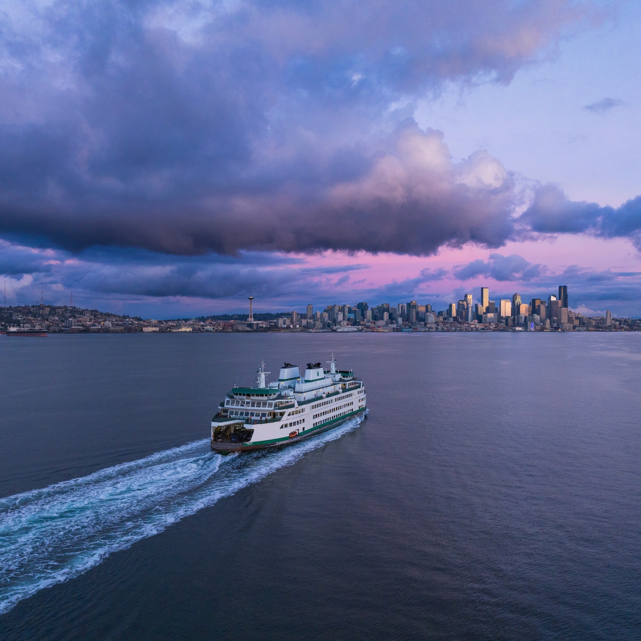 Aerial view of a Washington State Ferry crossing calm waters at dusk with the Seattle skyline in the background.