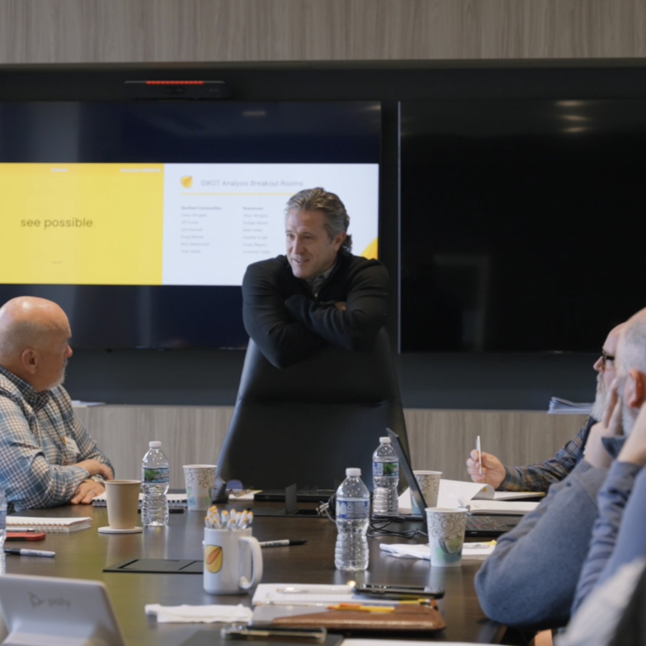 Speaker presenting on stage in front of a large orange-lit screen.
