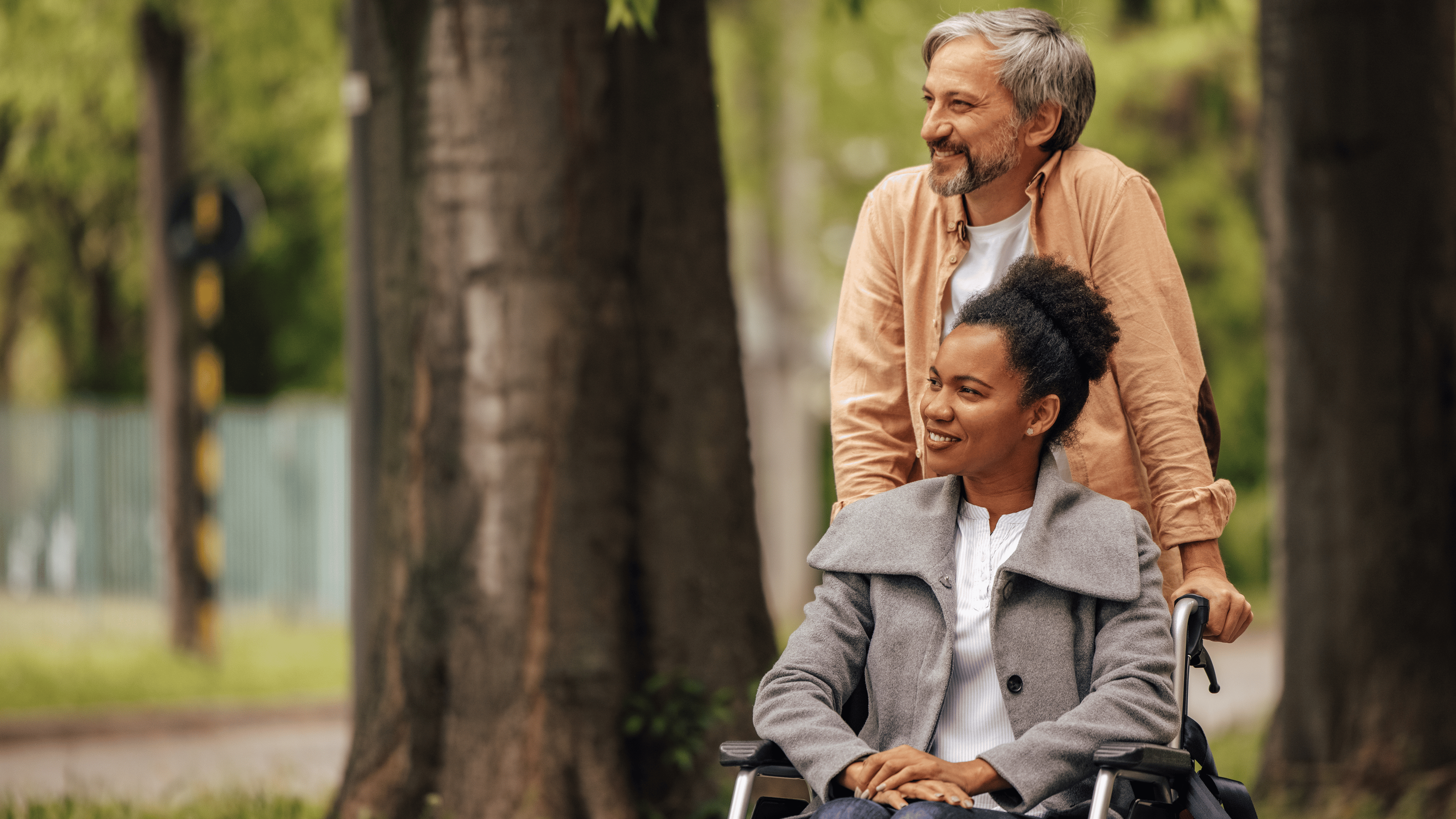 Adult man walking and pushing wheelchair in which woman is sitting.