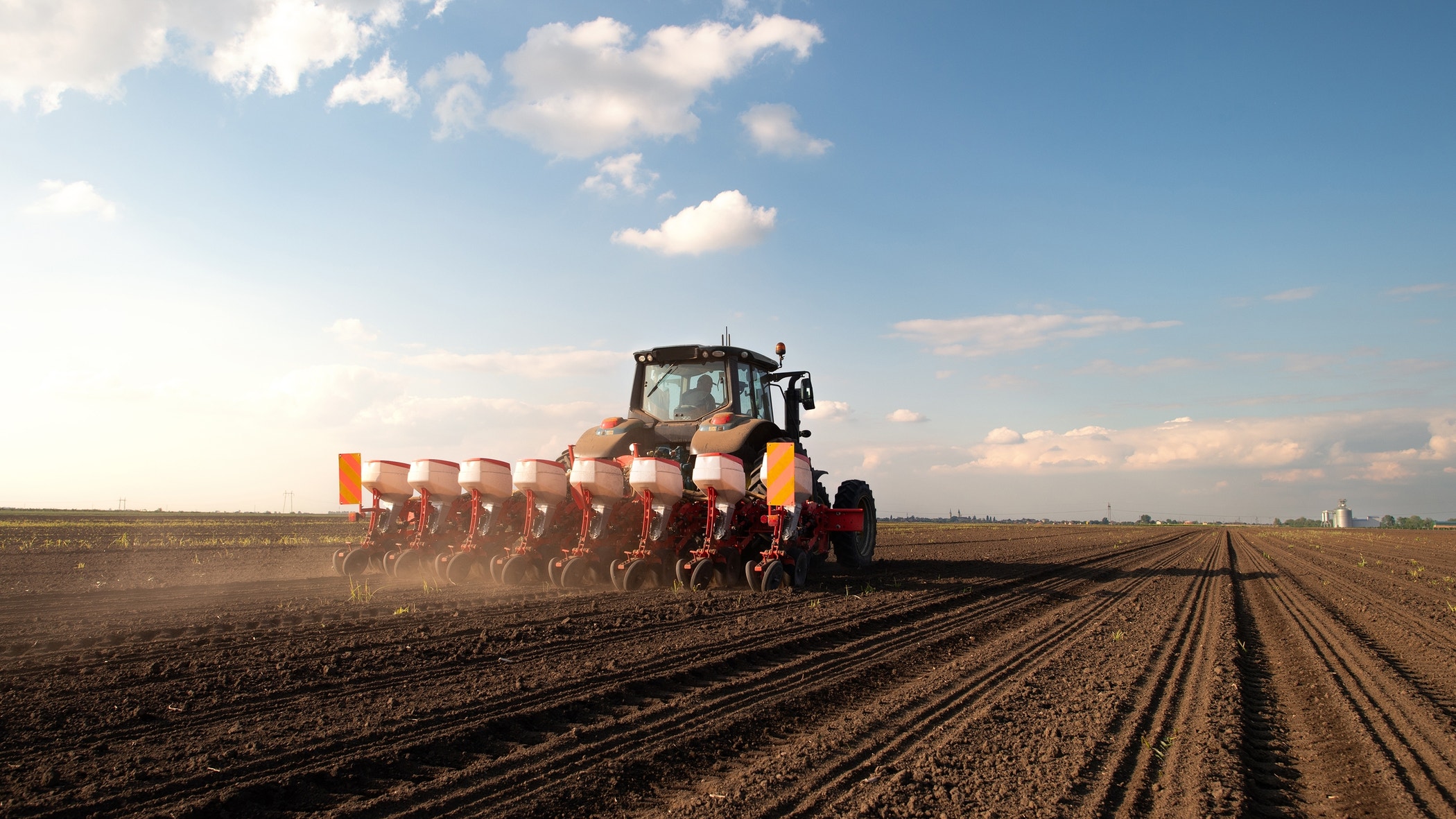 Farmer with tractor seeding - sowing crops at agricultural field. Plants, wheat.