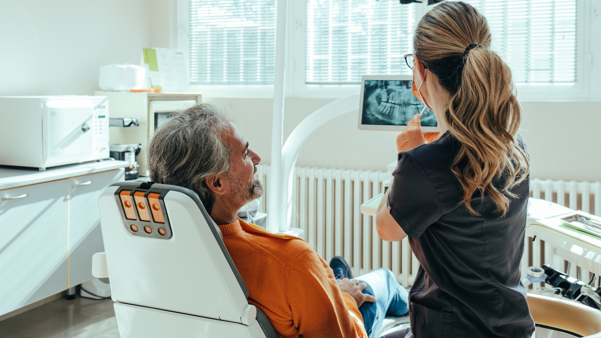An anonymous female dentist explaining teeth x-ray on a digital tablet to smiling mature patient at dentist's office.