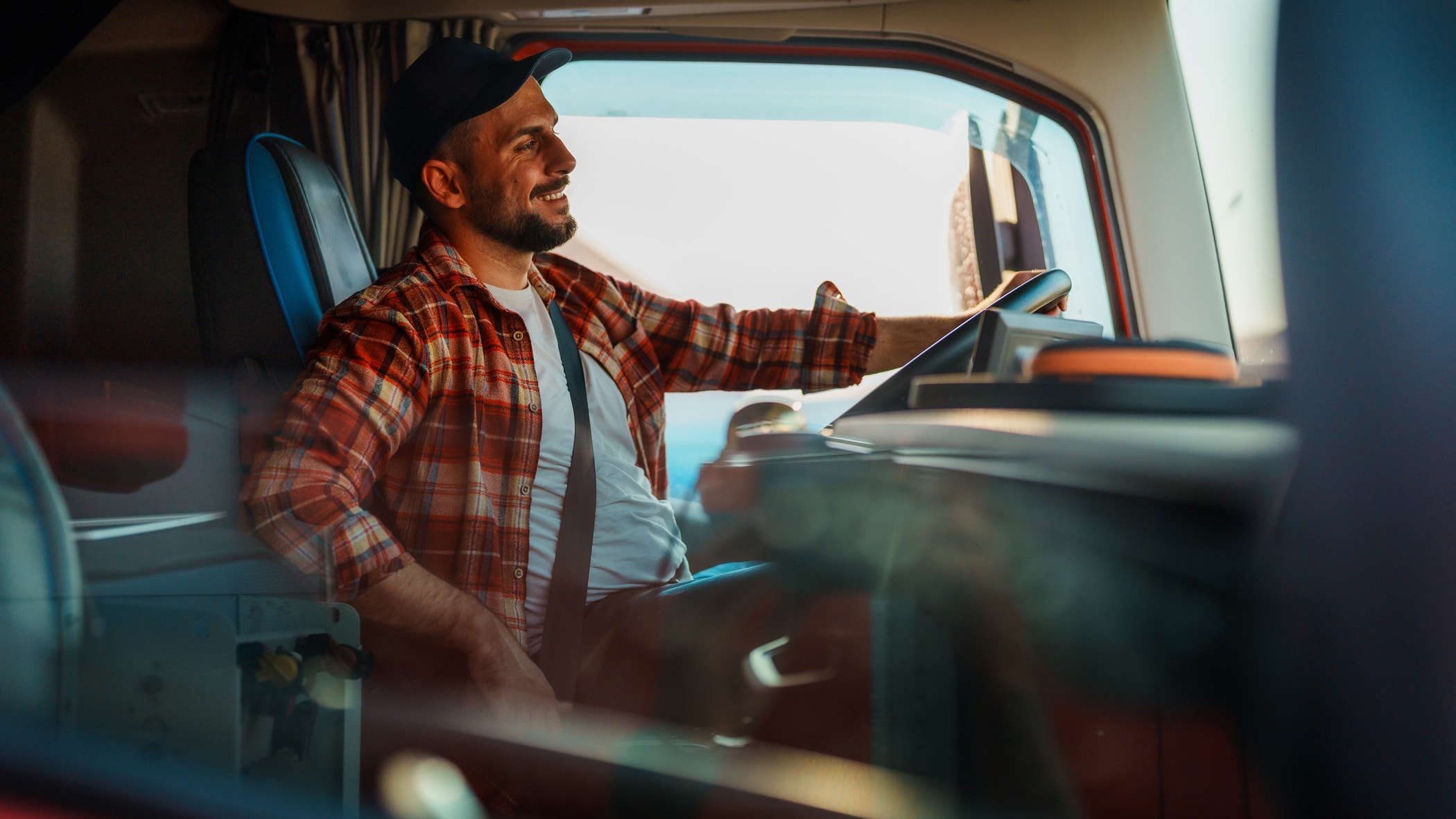 A professional truck driver with a heat and in plaid shirt fastening seat belt before starting a new trip.