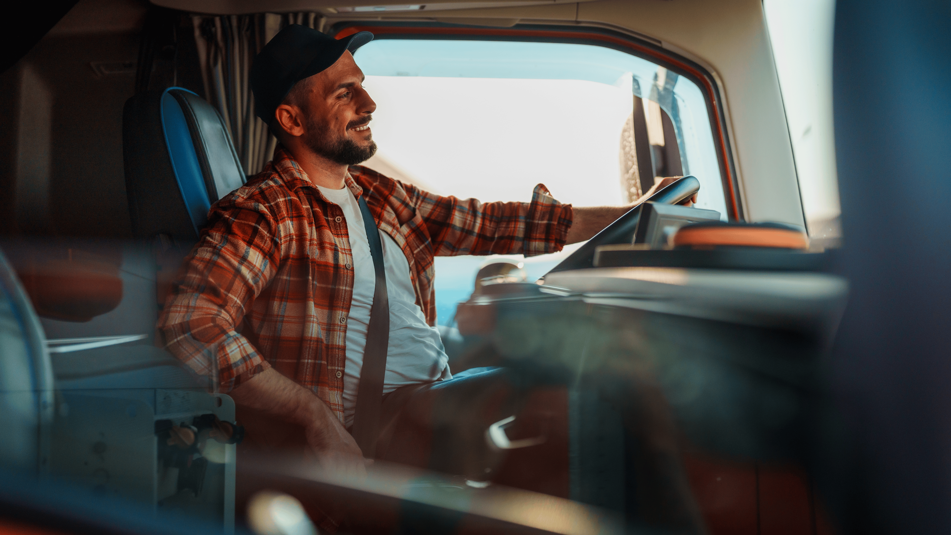A professional truck driver with a heat and in plaid shirt fastening seat belt before starting a new trip.