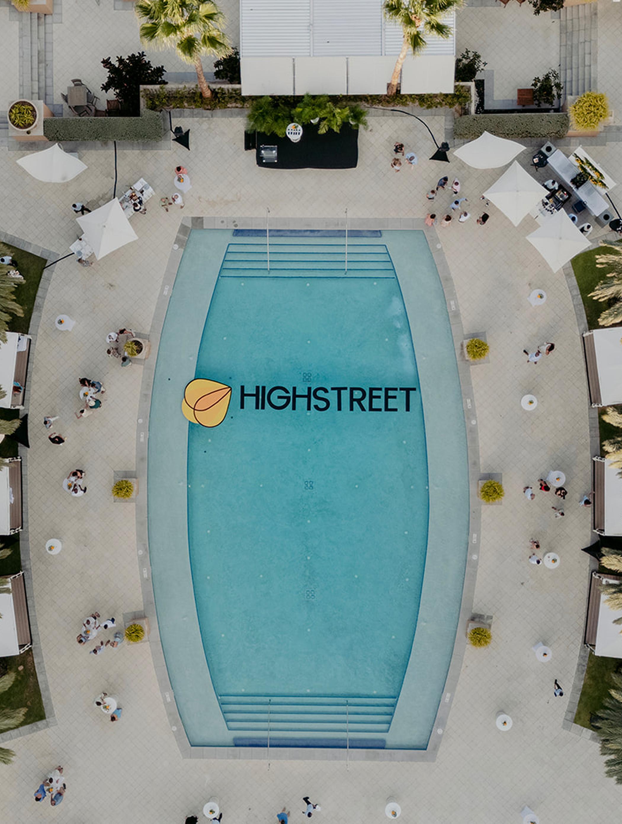 Two people smiling on a boat wearing shirts and caps with the Highstreet logo, standing over turquoise water on a sunny day.