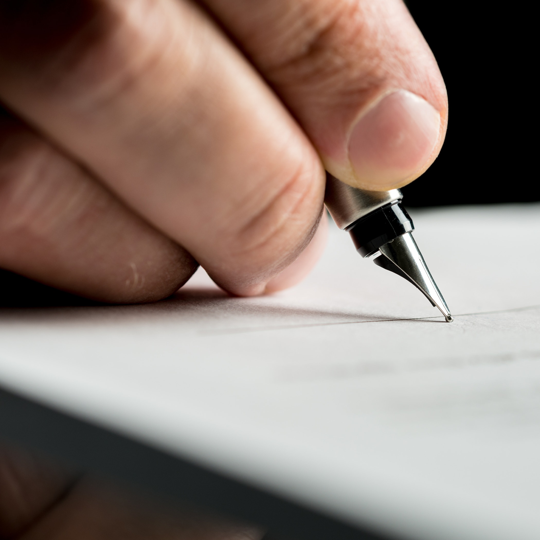 Macro shot of a hand of a businessman signing or writing a document on a sheet of white paper using a nibbed fountain pen.