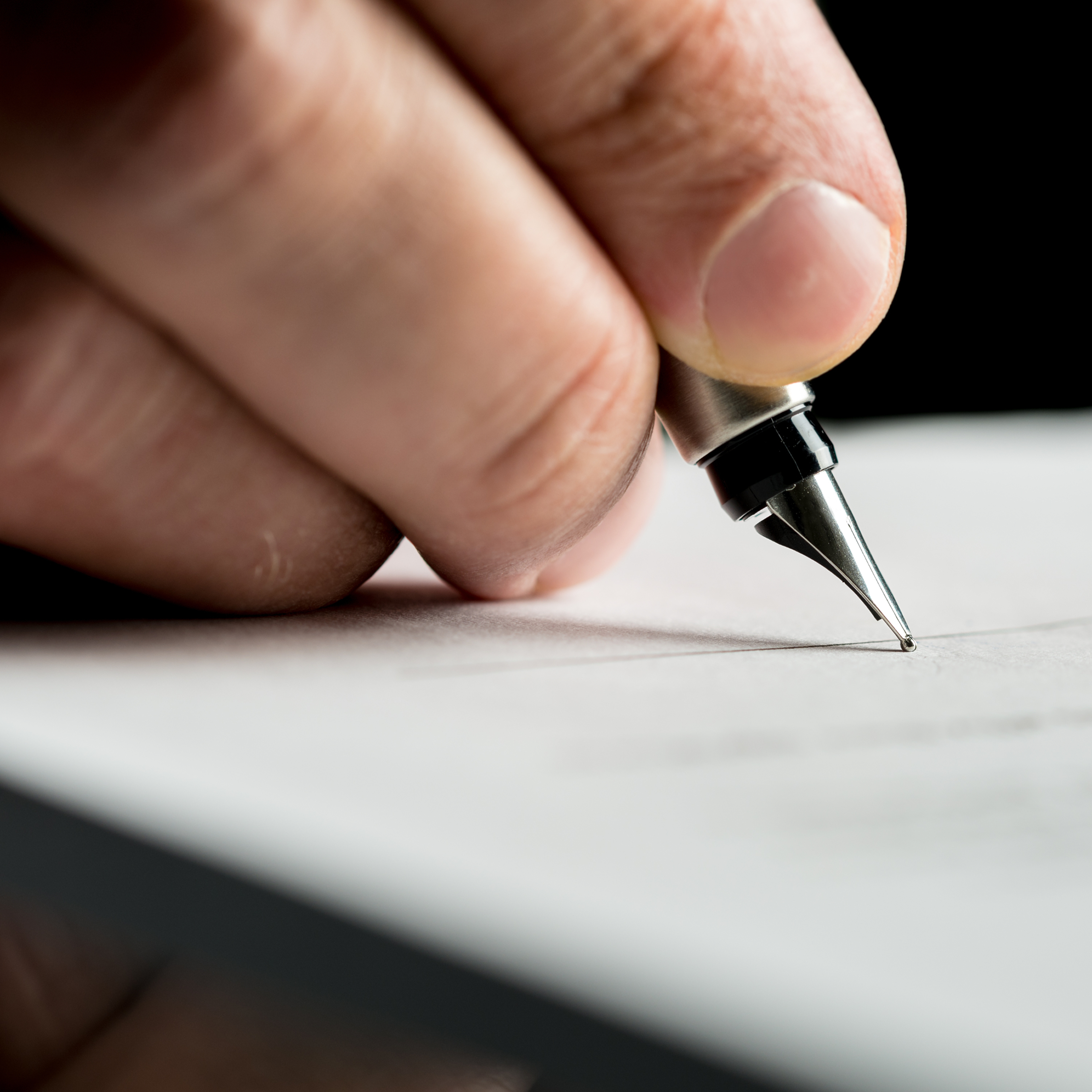 Macro shot of a hand of a businessman signing or writing a document on a sheet of white paper using a nibbed fountain pen.