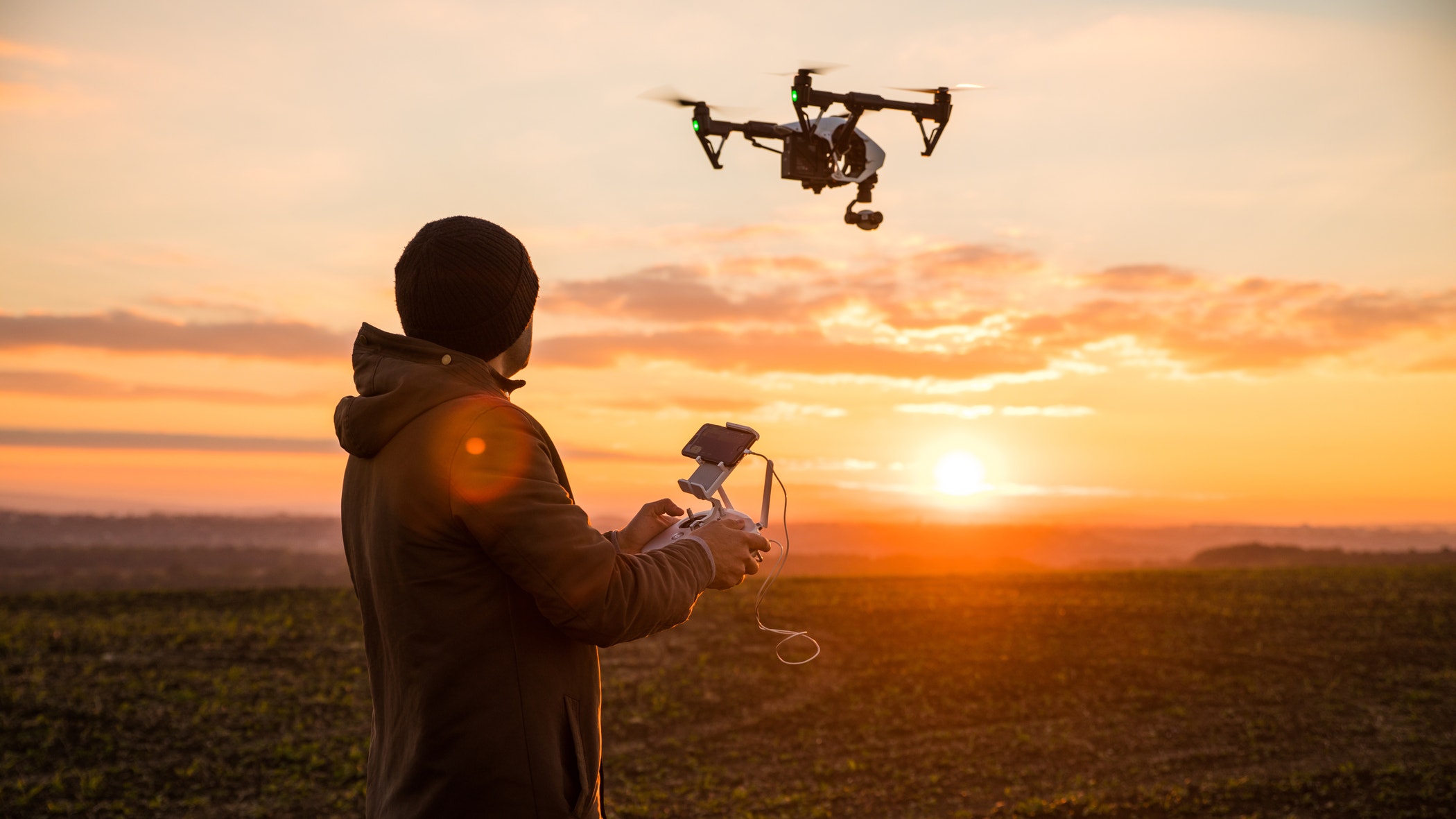 Man operating a drone with remote control. Dark silhouette against colorful sunset.