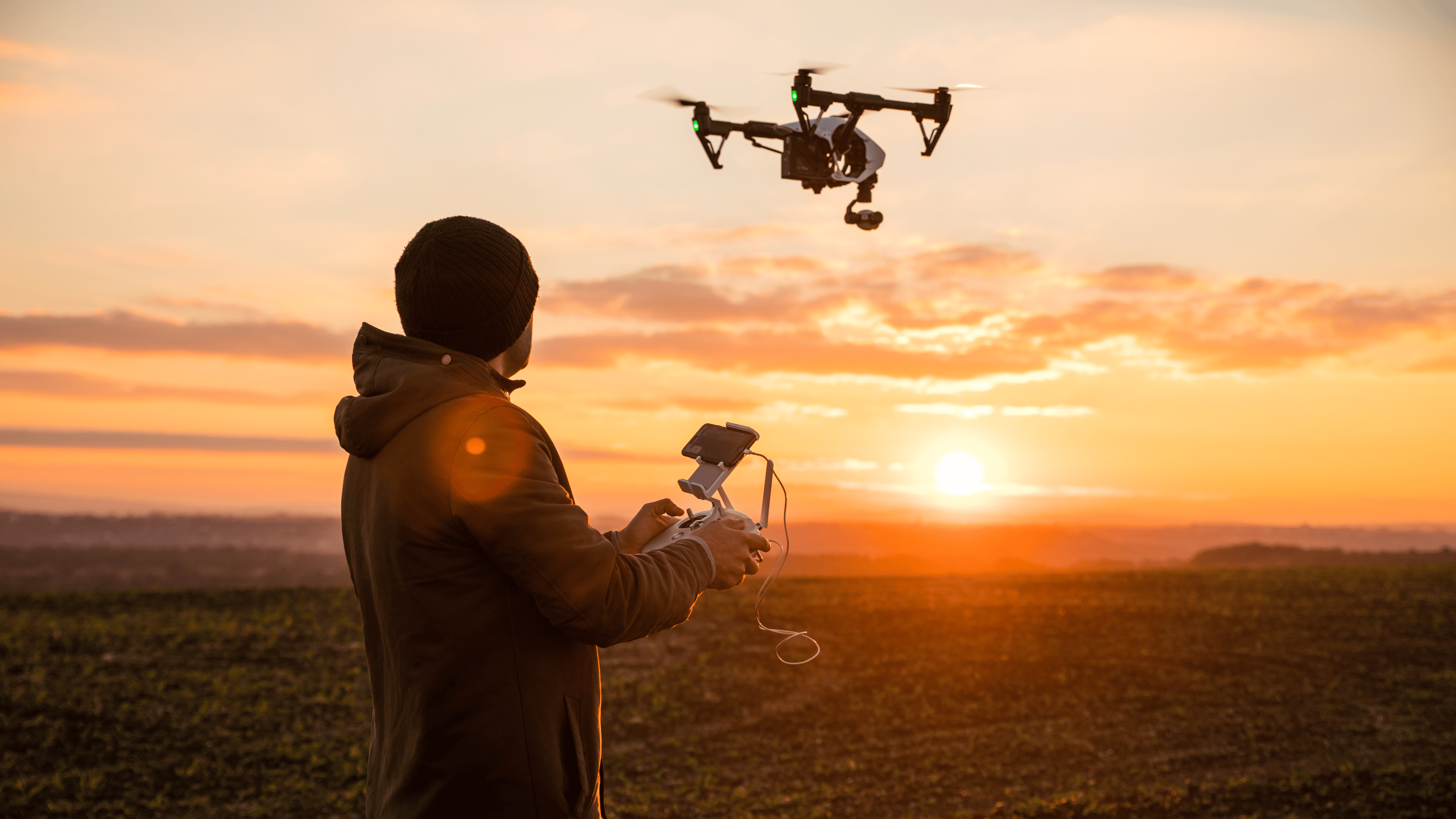 Man operating a drone with remote control. Dark silhouette against colorful sunset.