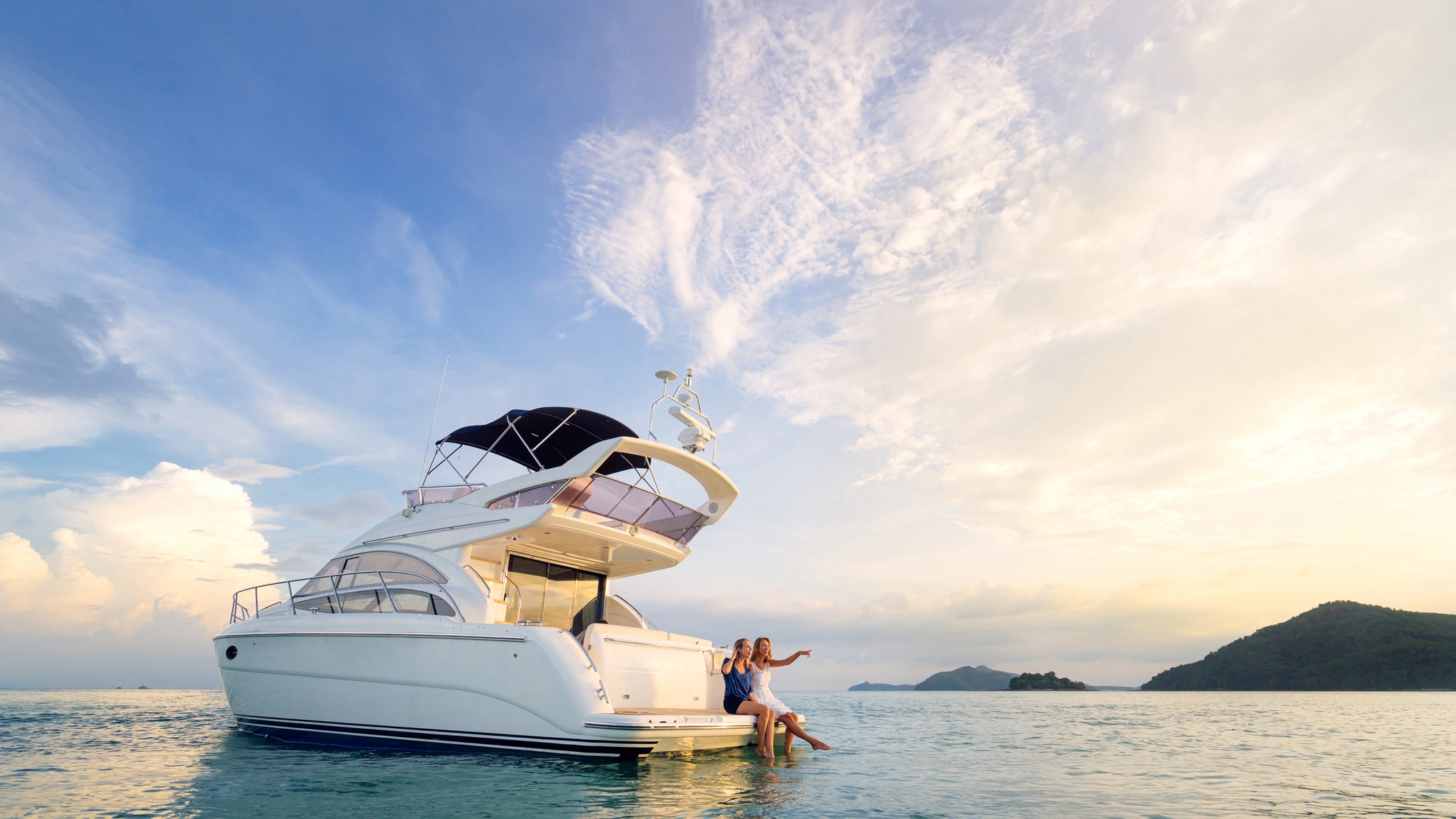 Friendship and luxury vacation. Two happy young women sitting on the yacht deck looking and pointing away sailing the sea.