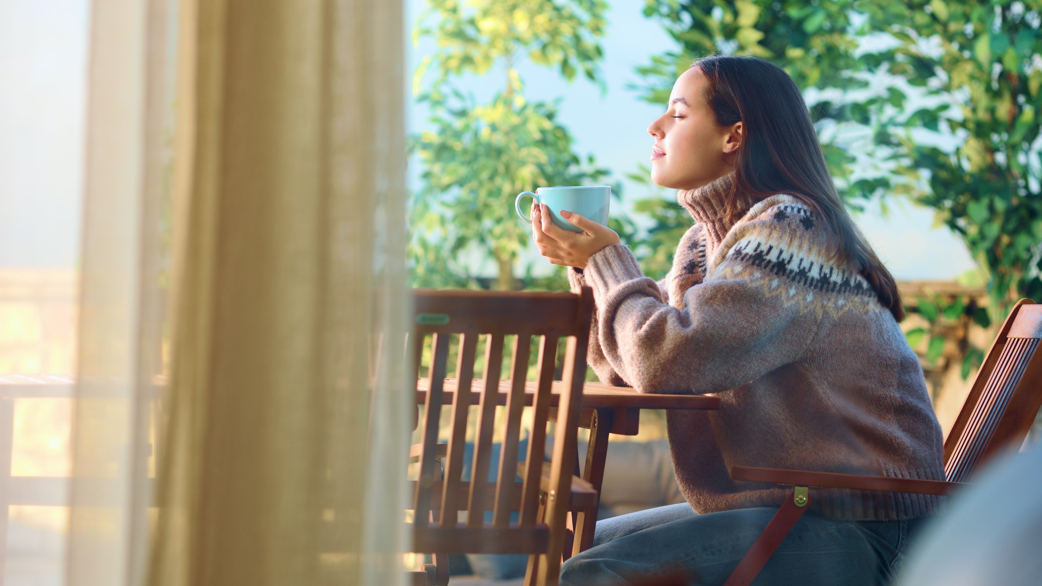 Side view portrait of a woman sitting in a terrace relaxing and drinking coffee at home.