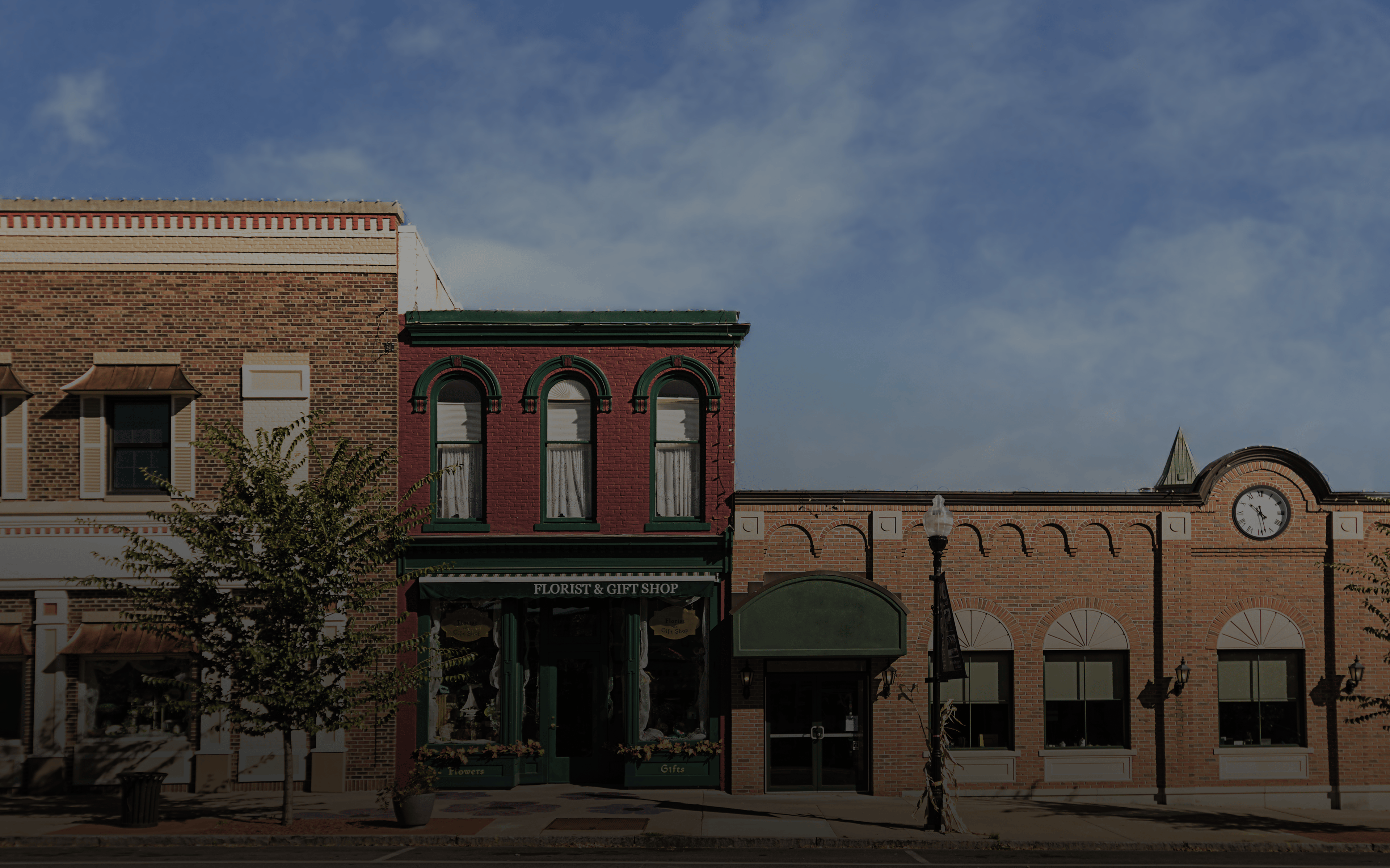 A photo of a typical small town main street in the United States of America. Features old brick buildings with specialty shops and restaurants. Decorated with autumn decor.