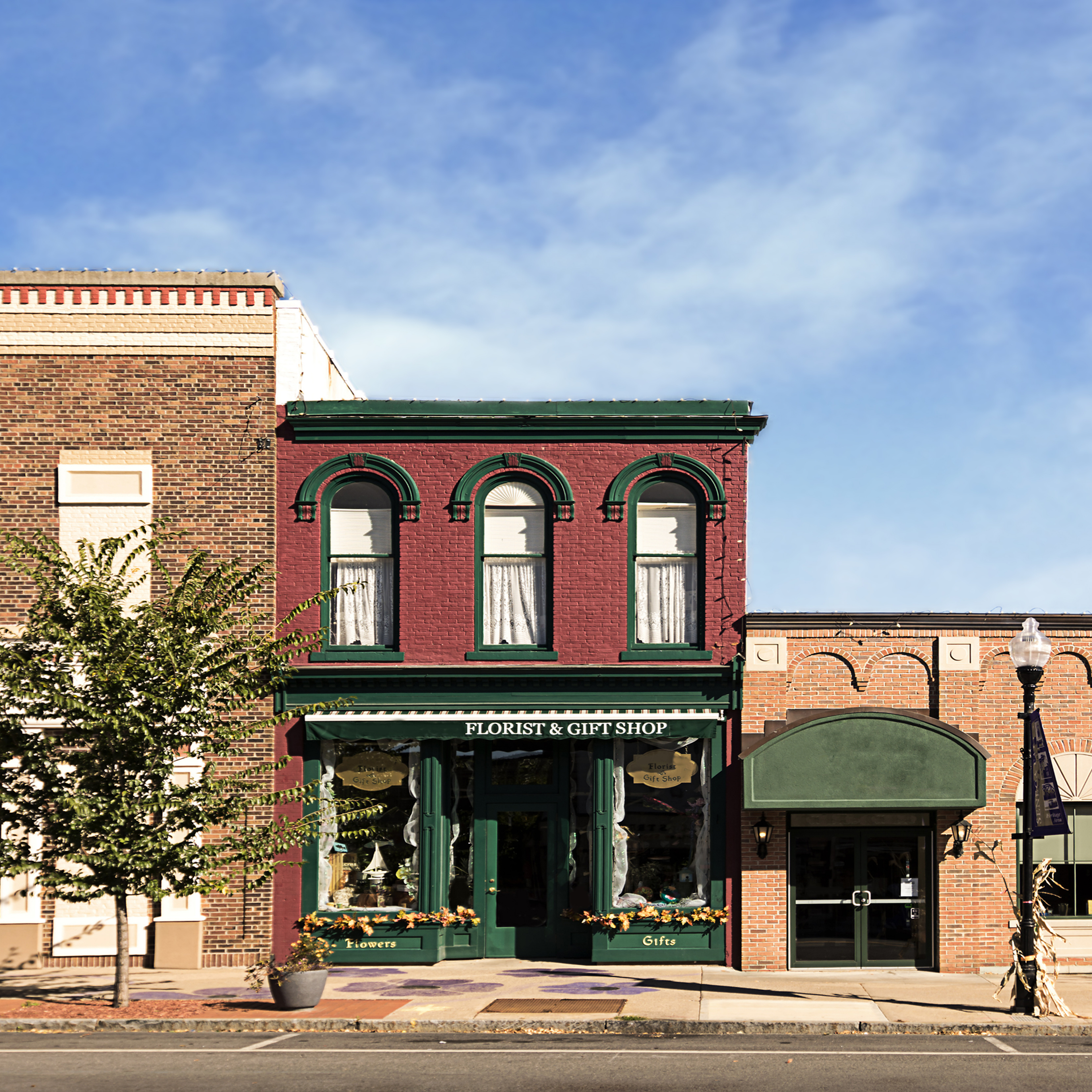 A photo of a typical small town main street in the United States of America. Features old brick buildings with specialty shops and restaurants. Decorated with autumn decor.