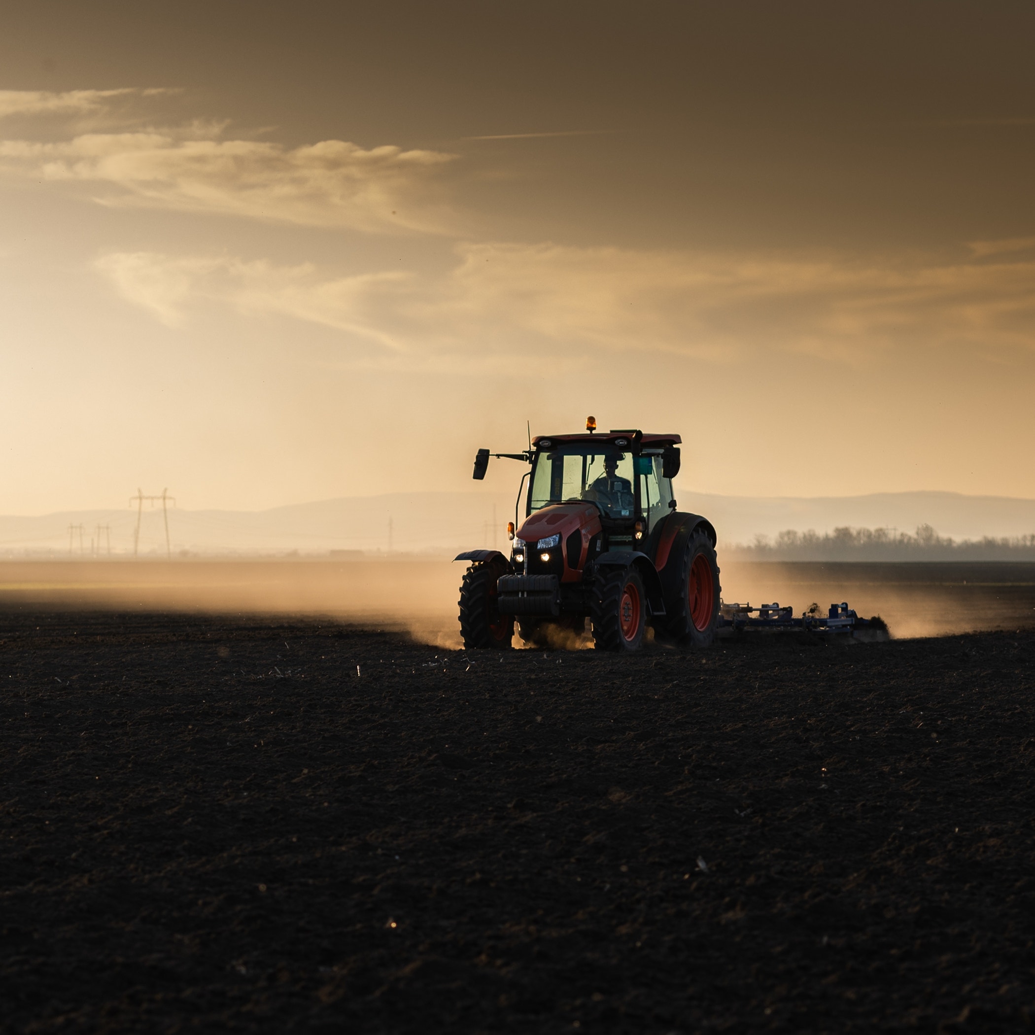 Tractor plowing farm preparing soil for new crop plantation during the evening.