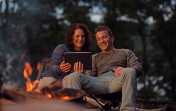 Two people by a campfire looking at a tablet