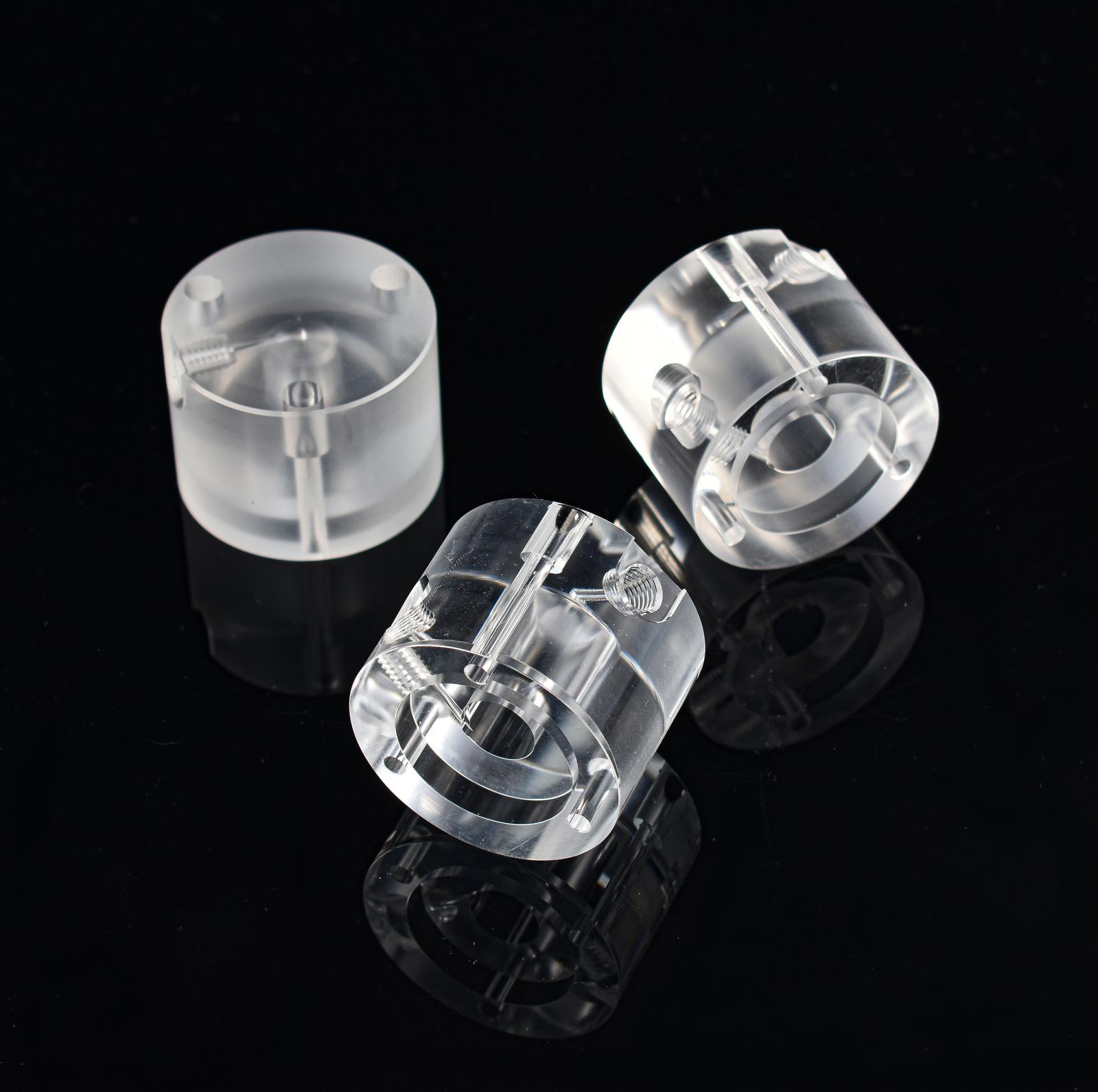 Three transparent acrylic cylinders, two upright and one tilted, are placed on a glossy black surface, highlighting their graduating smooth texture and reflective quality.