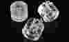 Three cylindrical clear acrylic components with precision-machined holes and polished surfaces, displayed on a reflective black background.