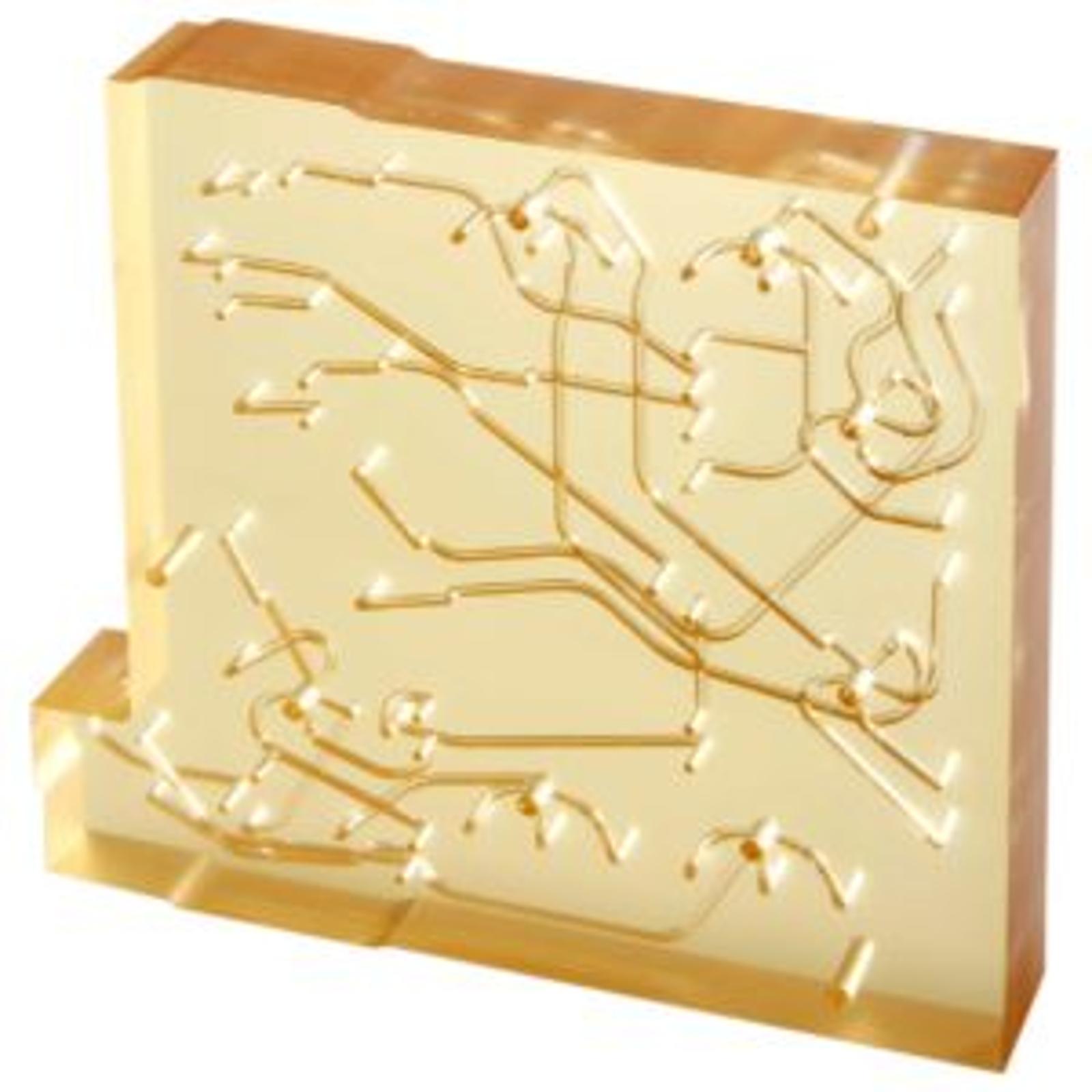 A translucent polysulfone microfluidic manifold resembling an abstract circuit or network pattern, viewed at an angle on a white background.