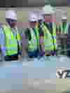 A group of men wearing safety vests and safety hard hats standing next to yz odorizer