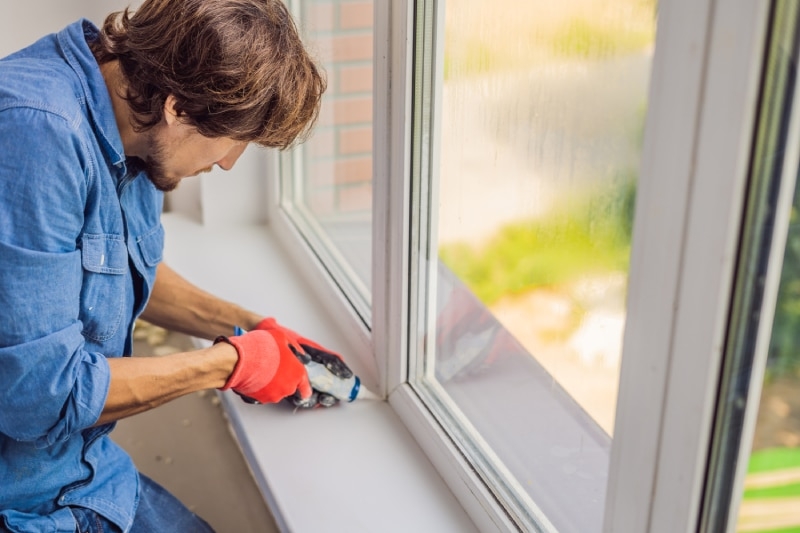 man caulking his window in his home