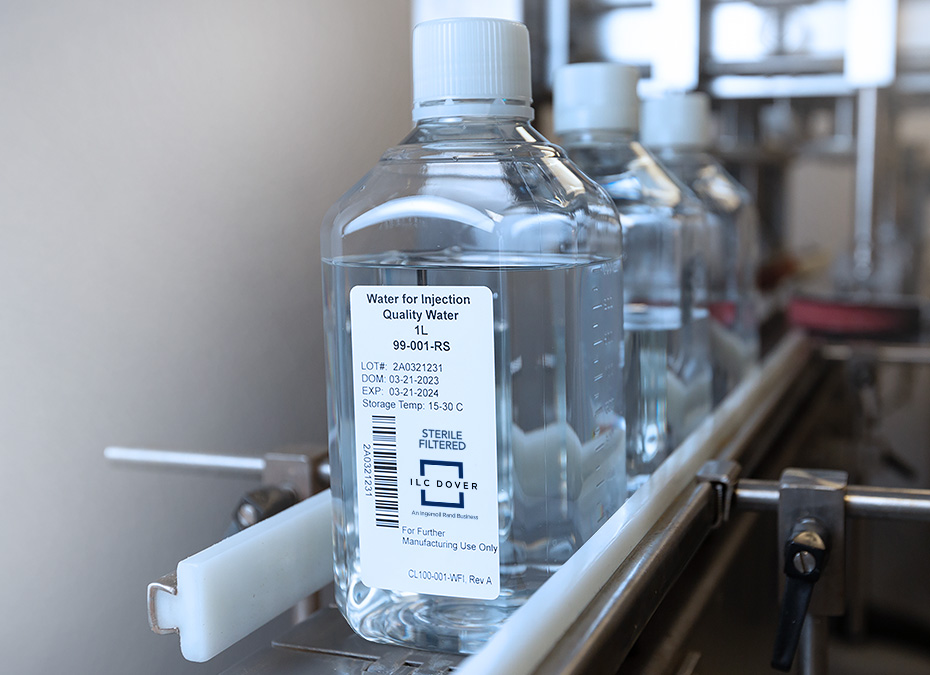 Bottle labeled 'Water for Injection' on a conveyor in a manufacturing or lab setting.