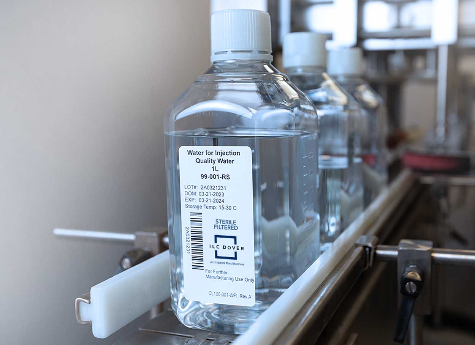 Bottle labeled 'Water for Injection' on a conveyor in a manufacturing or lab setting.