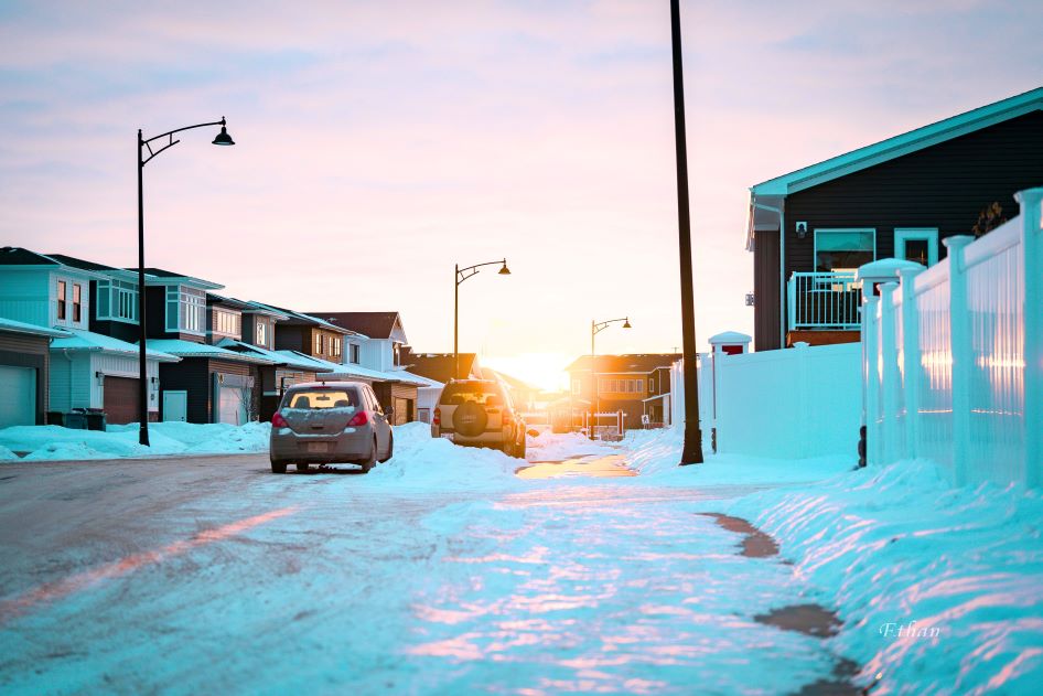 The sun peaks through a row of homes. There's snow on the ground, with items properly stored in Canada. 