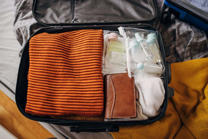 Top view of an open suitcase — with articles of clothes, a wallet, and toiletries — being used as an essentials bag during a move.