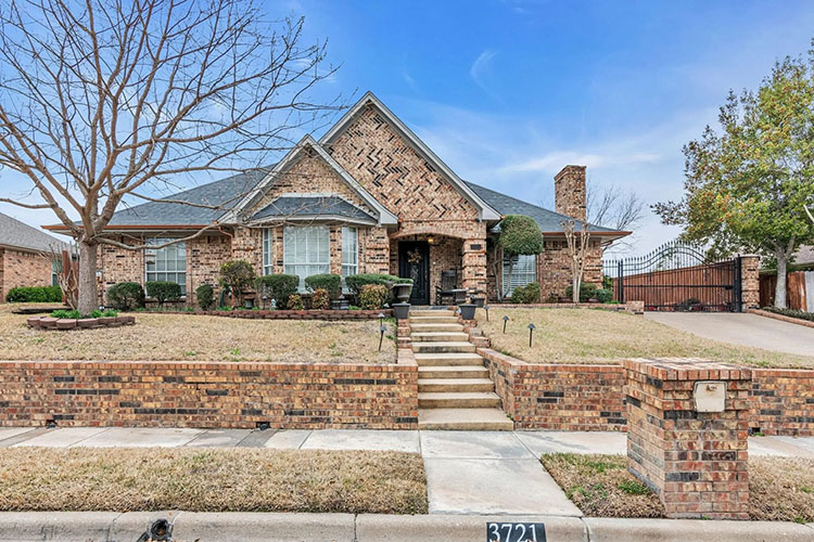 A multi-story stone home in Bedford, Texas. There is a stone wall lining the stairs leading up to the home. A bare tree is off to the left of the image. 