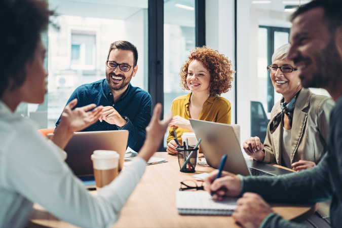 A diverse group of office workers are laughing together at a conference table during a business meeting.
