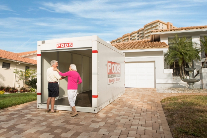 A happy elderly couple stands in their driveway beside an empty PODS portable moving container, ready to relocate after years of thinking of retiring somewhere warm.