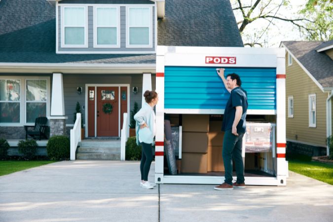 A couple prepares to close their loaded PODS moving container in the driveway of their new home after saving on moving costs with a hybrid move.