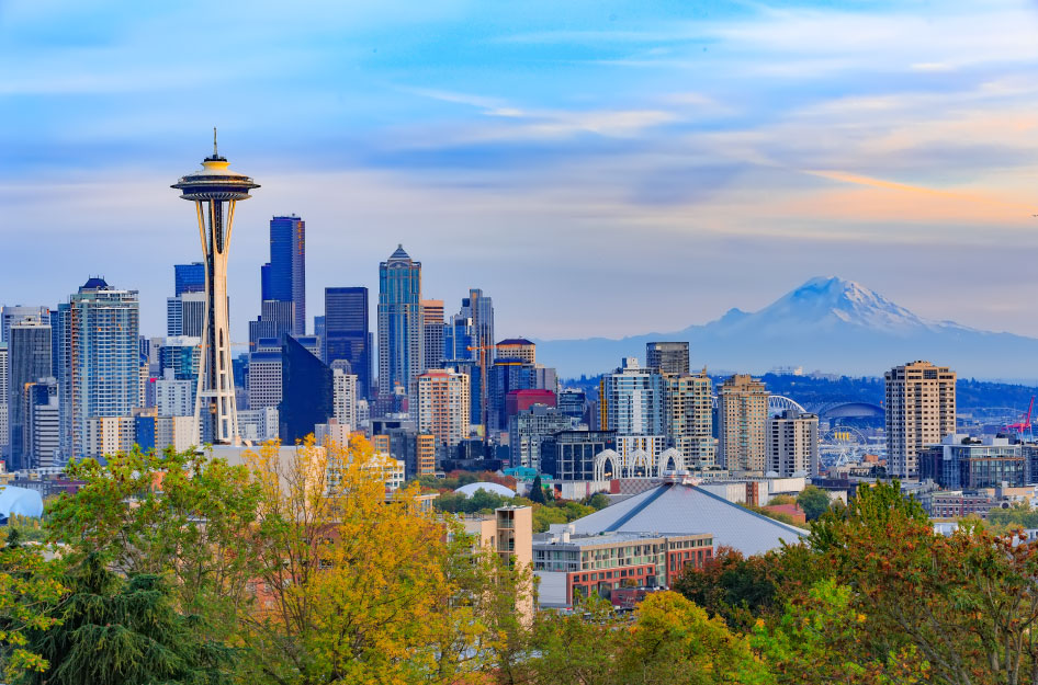 A distant view of the Space Needle and Downtown Seattle with a blue skyline and mountain in the background.